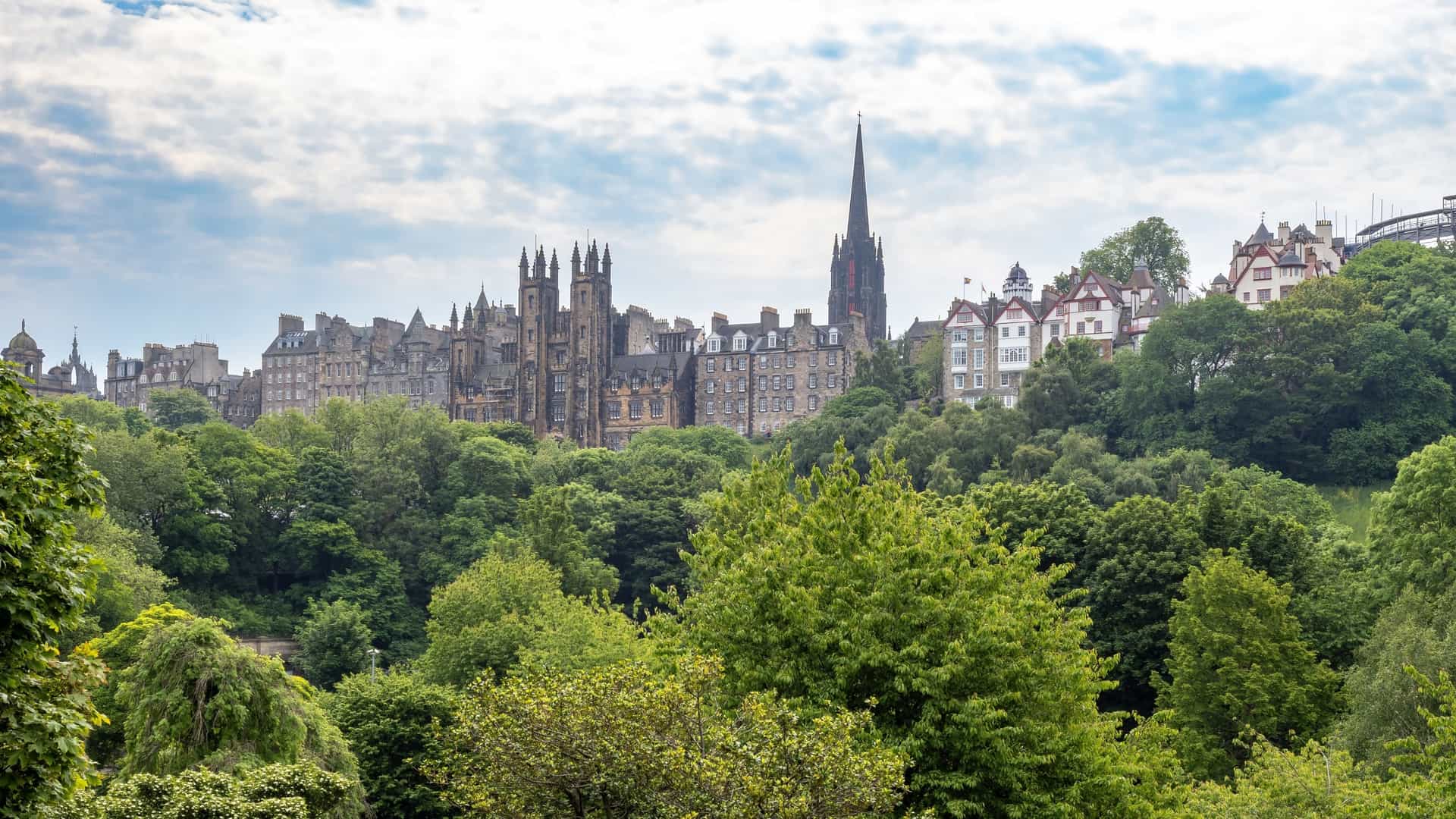  A scenic view of Princes Street Gardens in Edinburgh, Scotland. The image shows the green expanse of the park, with well kept lawns and trees in the foreground. In the background, the cityscape of Edinburgh's Old Town rises above, with its historic buildings and prominent landmarks visible against the skyline. The image captures the contrast between the tranquil park and the bustling urban environment.