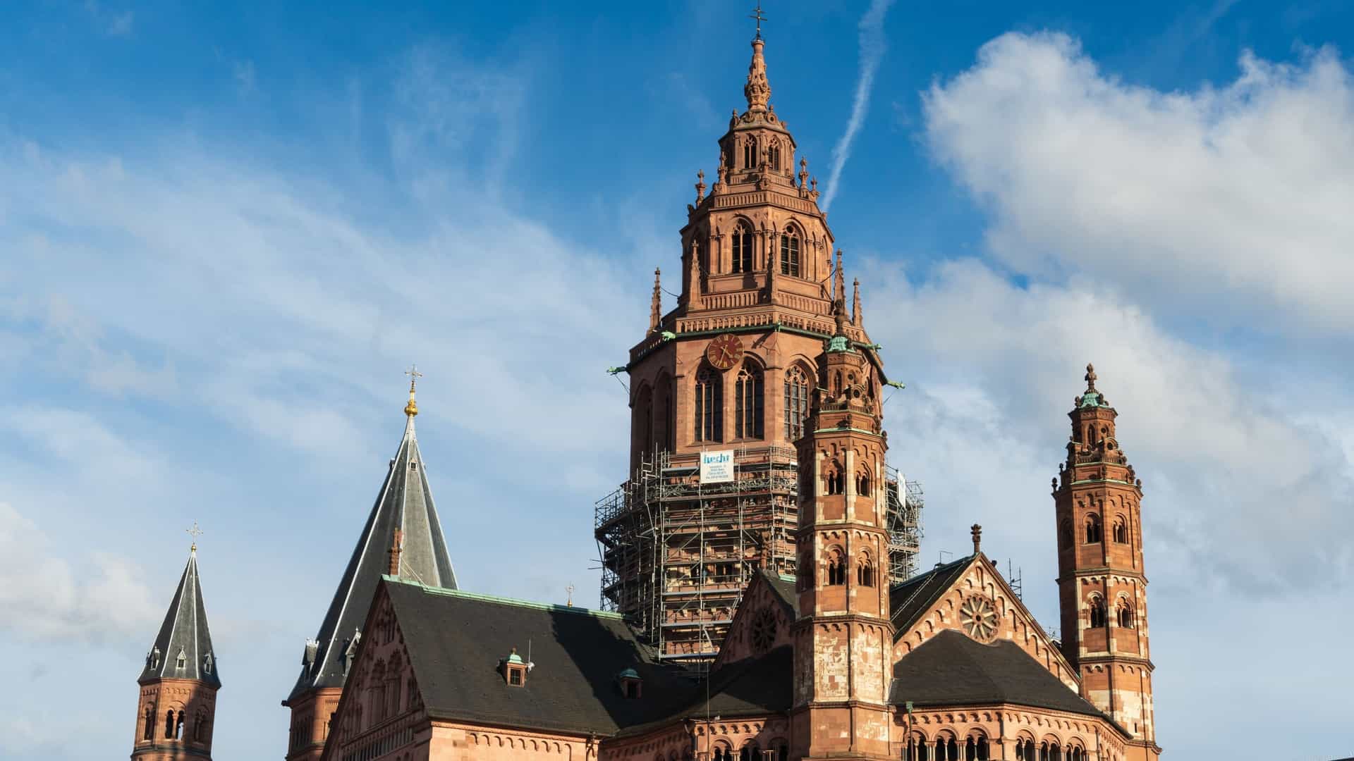 A view of the city of Mainz, Germany, situated along the Rhine River, showing a bridge and cityscape under a clear sky.