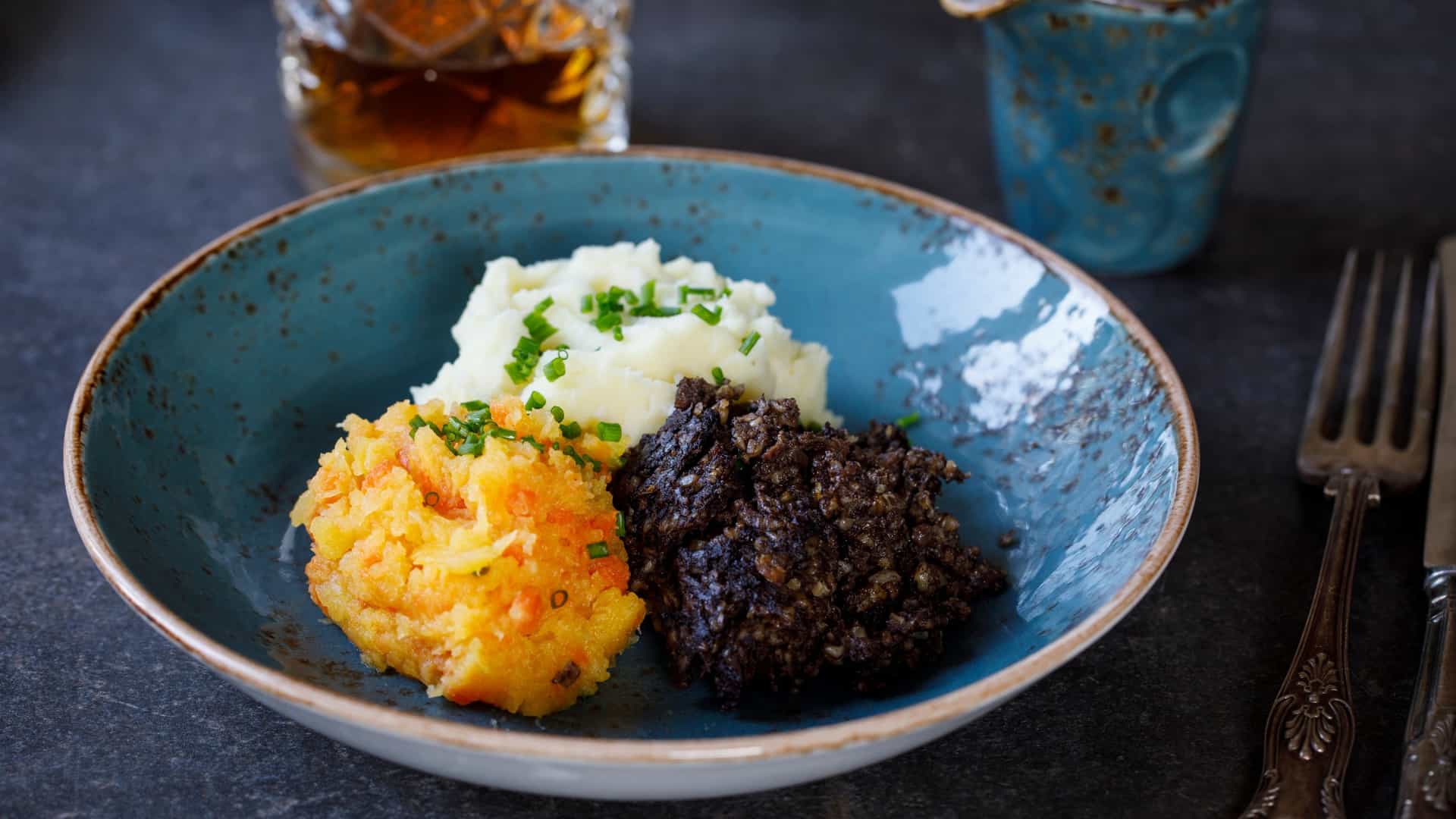  A traditional Scottish meal of haggis, neeps, and tatties is presented on a plate. The haggis, a savory pudding, is served alongside a portion of mashed turnips ("neeps") and a portion of mashed potatoes ("tatties").