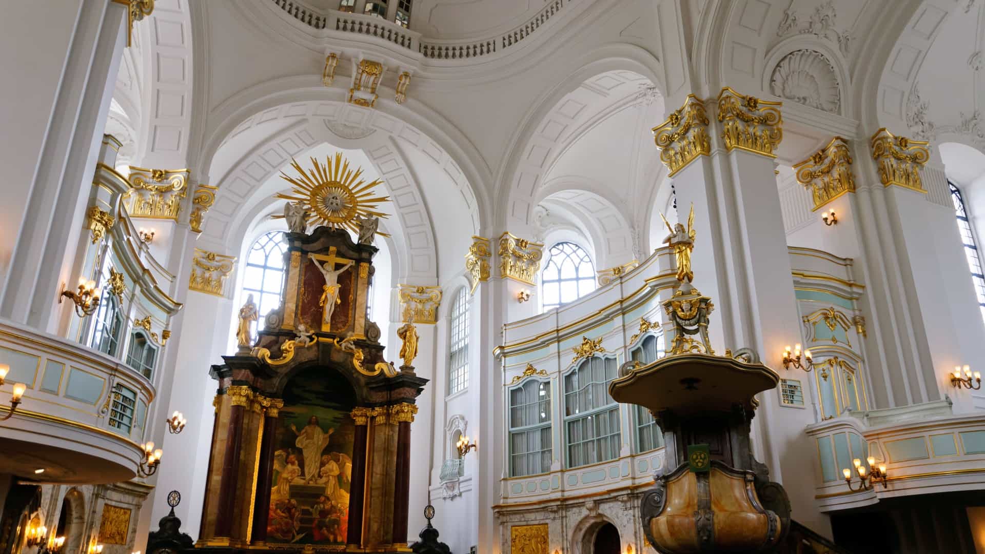  A low angle, close up photograph of St. Michael's Church, or "Michel," in Hamburg, Germany. The Baroque style church is a landmark of the city. The image focuses on the facade, highlighting the intricate details of the brick and stone work, with a portion of its distinctive spire visible against a bright sky.
