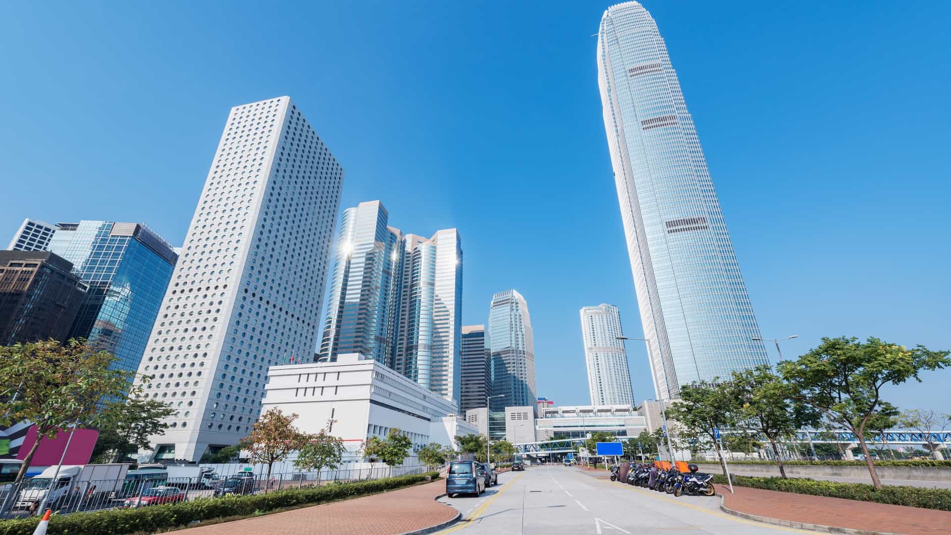 A daytime view of a bustling street scene within the Central Business District of Singapore. The image features modern skyscrapers, contemporary office buildings, and busy road traffic, capturing the dynamic and high-density urban environment of the city's financial heart.