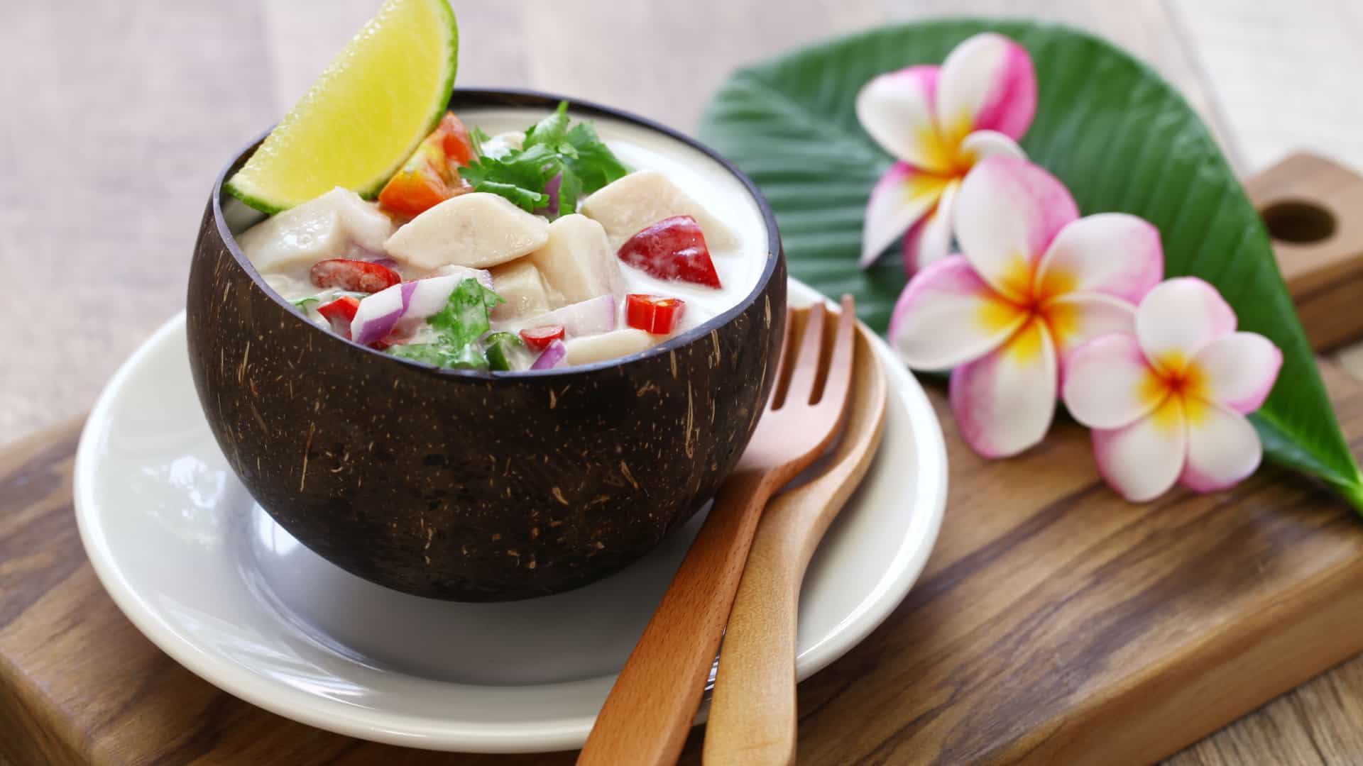 A close-up, top-down view of Kokoda, a traditional Fijian ceviche dish. The dish consists of cubes of raw fish (like snapper or mahi-mahi) marinated in lime juice and then mixed with coconut milk (miti), diced vegetables like red onion, cucumber, and chilies. The creamy, white dish is brightly colored by the fresh vegetables and is often served chilled in a decorative bowl or a coconut shell.