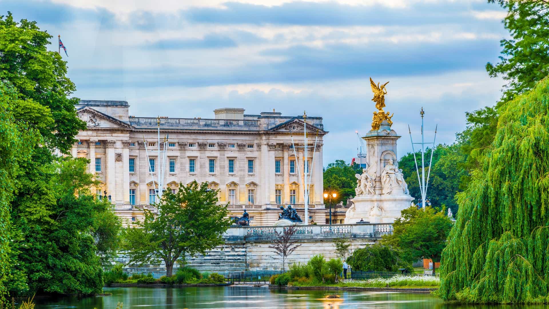  Buckingham Palace, the official London residence of the monarch, is viewed from St. James's Park. The image shows the palace's facade and the Victoria Memorial in the foreground, with the park's serene landscape and a lake visible.