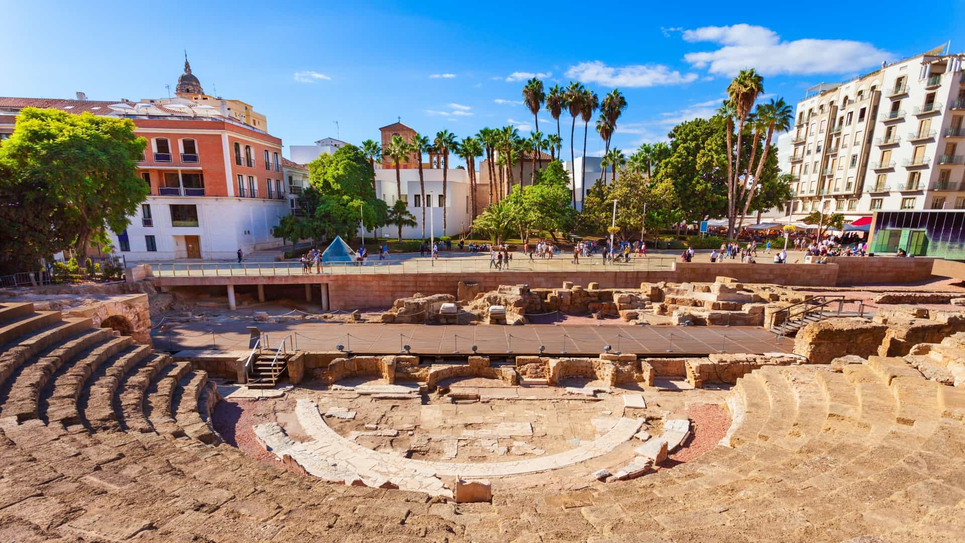  A view of the Roman Theatre (Teatro Romano de Málaga) in Málaga, Spain. The image shows the ancient archaeological site with its well preserved tiered seating, or cavea, and the orchestra area. The theater is situated at the foot of the Alcazaba fortress, which is visible in the background. The scene highlights the contrast between the ancient Roman ruins and the more modern structures of the city.
