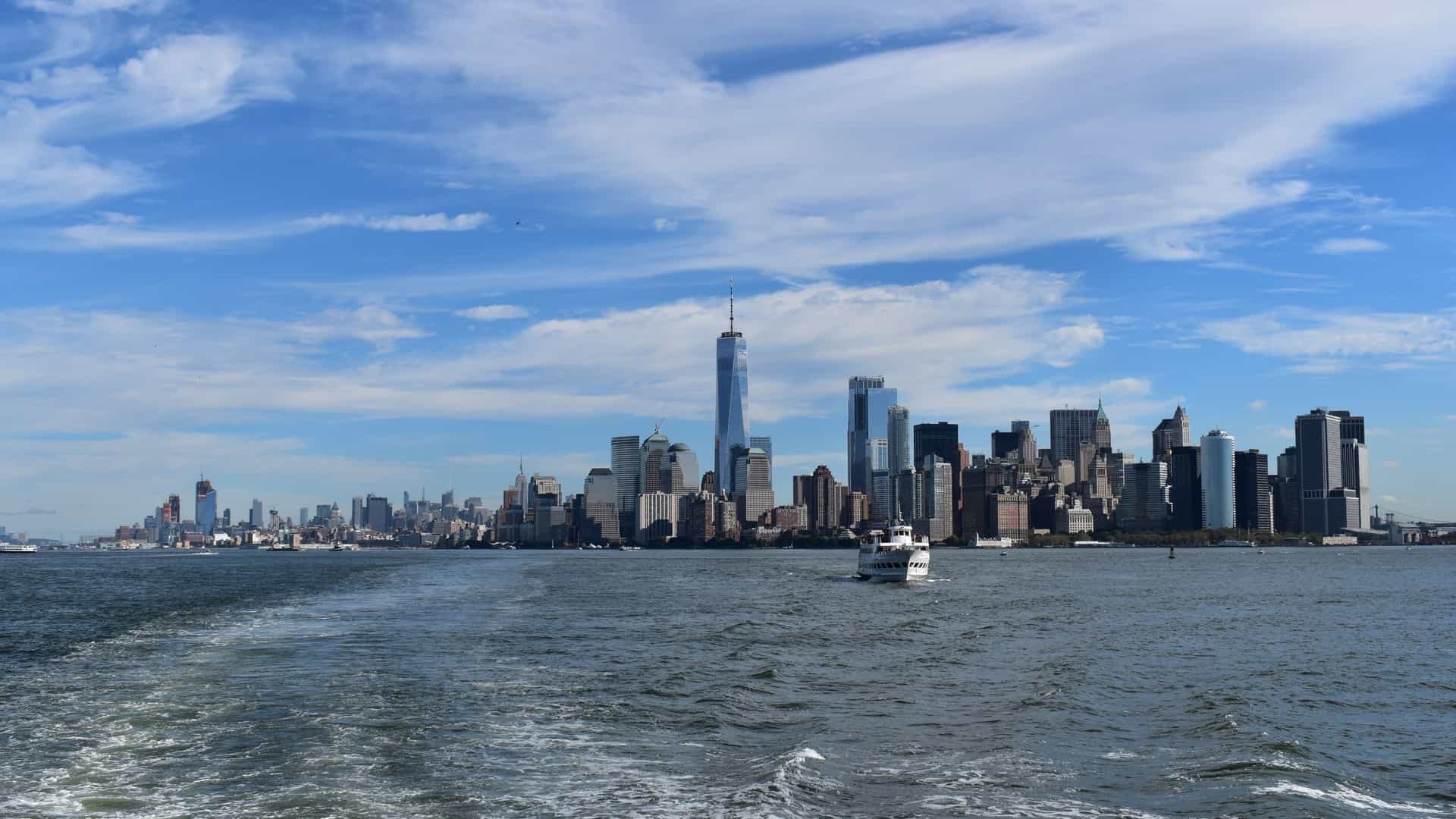 A stunning, illuminated panoramic view of the Manhattan skyline at sunset, seen from the perspective of the Hudson River. The vibrant skyscrapers of Midtown and Downtown, including the Empire State Building, are perfectly framed—the ideal view when you Take a Circle Line Sightseeing Cruise.