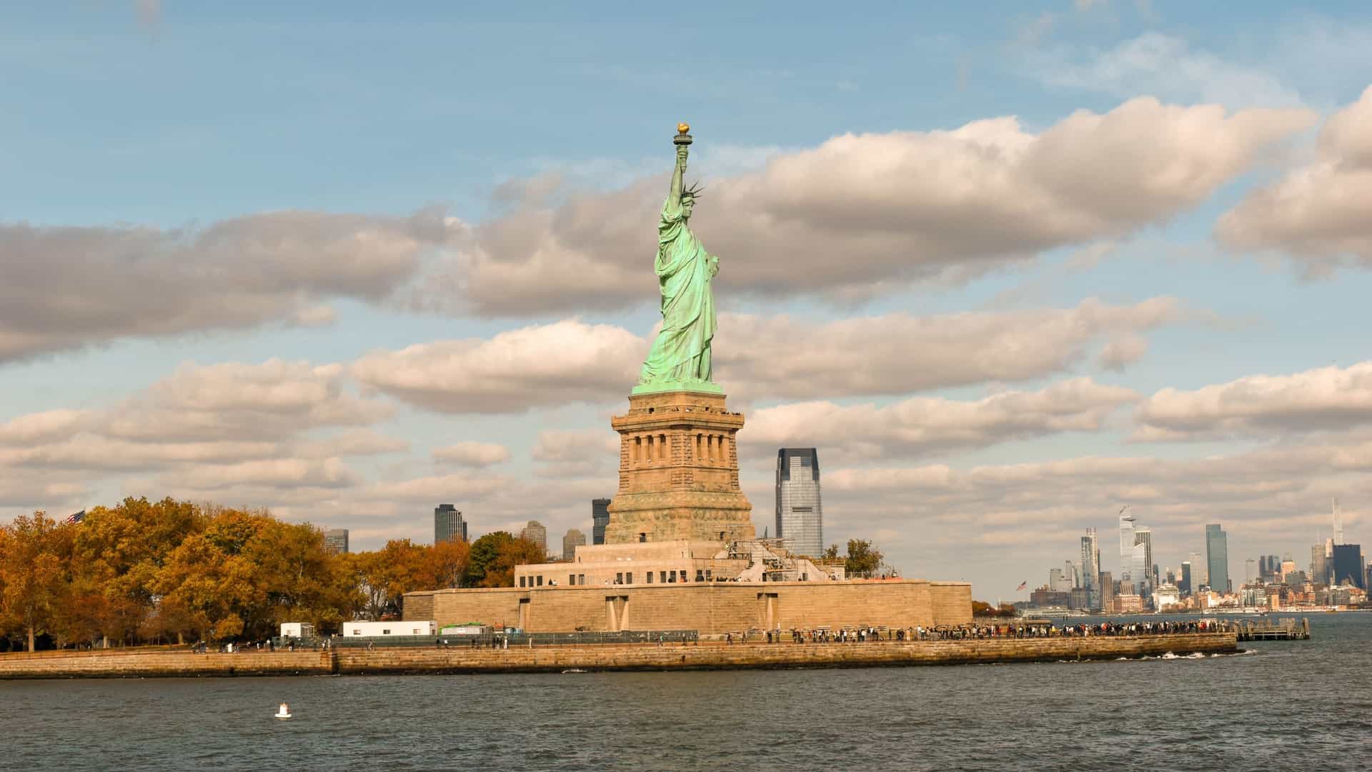 The Statue of Liberty is dramatically framed through the window of a moving boat or ferry, highlighting the view that passengers enjoy on their boat trip. The iconic green statue stands against the cityscape of New York and the water, capturing the essence of a harbor tour.