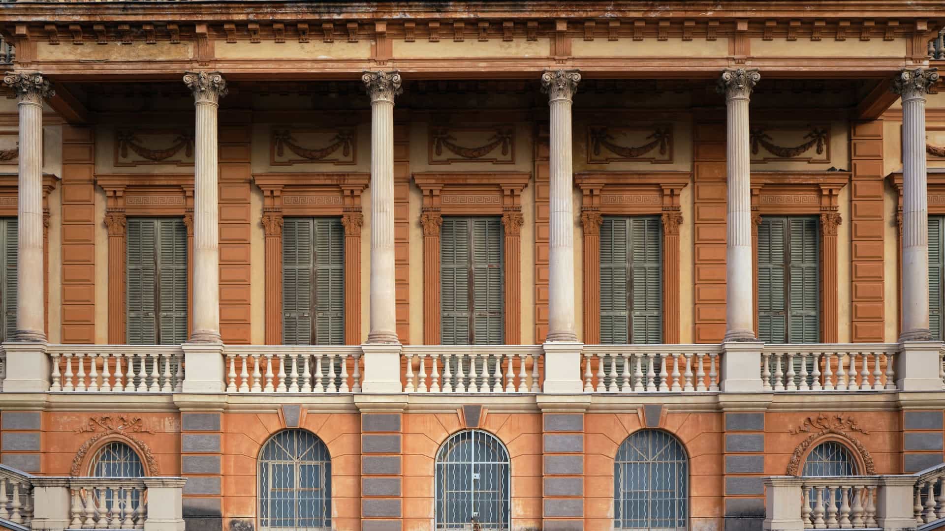 An exterior view of the Museum of Fine Arts (Musée des Beaux-Arts) in Nice, France. The museum is housed in a grand, two-story Italian Renaissance-style palace, recognizable by its salmon-colored stucco, large arched windows, and elaborate decorative elements. The building is set amidst a manicured garden with palm trees and a lush lawn.