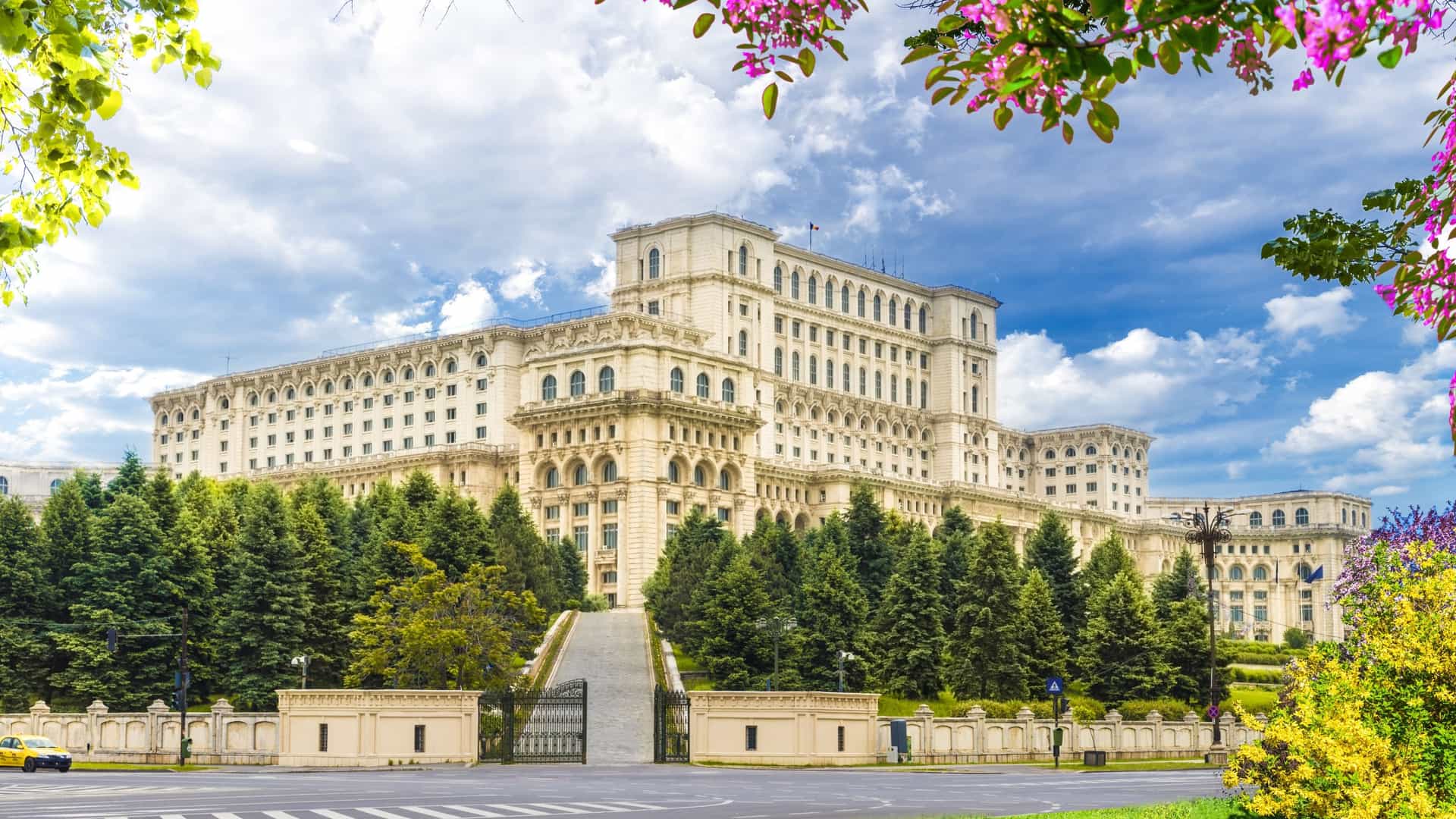 Palace of the Parliament in Bucharest, Romania. The massive neoclassical and socialist realism administrative building, also known as Casa Poporului (People's House), stands prominently under a clear blue sky.