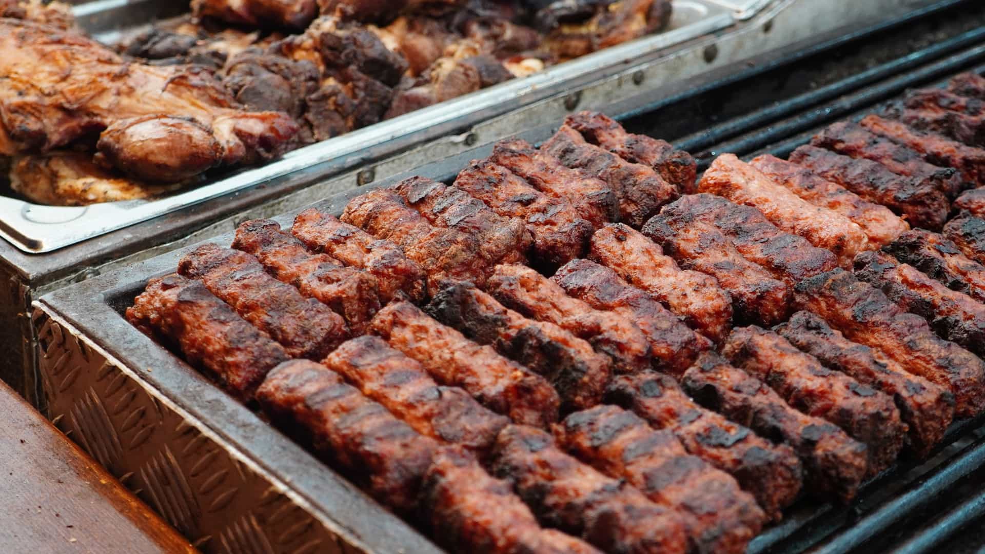  A close up shot of several traditional Romanian grilled minced meat rolls, known as "mici" or "mititei," placed on a bed of fresh, chopped onions. The rolls are golden brown and have distinct grill marks, indicating they were cooked over an open flame. A small dollop of yellow mustard is visible next to the rolls.