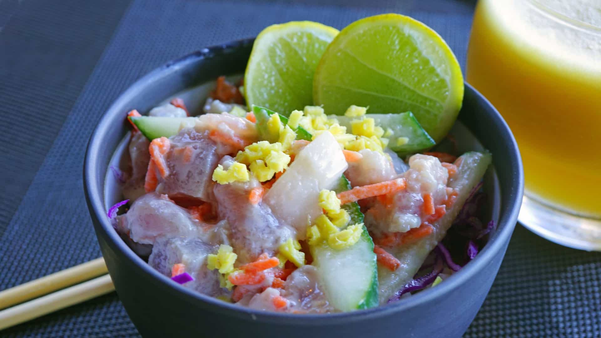 A close-up of a bowl of "Poisson Cru," the national dish of Tahiti and French Polynesia. It consists of cubes of raw tuna (or other firm, white fish) that have been marinated in fresh lime juice and then mixed with creamy coconut milk and diced vegetables such as cucumber, tomato, and red onion. The dish is presented in a bowl, showcasing its white, creamy sauce and colorful ingredients.