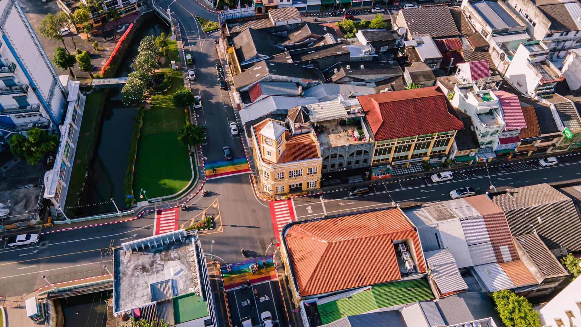 A lively nighttime view of the walking street in Phuket Old Town, Thailand, filled with the night market. The street is illuminated by string lights and the colorful glow from numerous food and souvenir stalls lining the sides. The background features well-preserved Sino-Portuguese architecture, with pedestrians filling the street browsing the market activity.