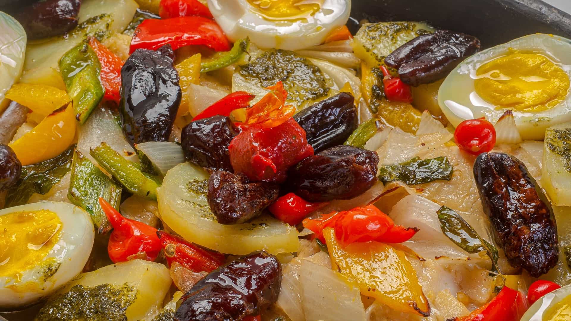 A prepared dish of Bacalhau à Gomes de Sá, a famous Portuguese cuisine. The casserole shows flaky salt cod (bacalhau) pieces mixed with potatoes, onions, hard boiled eggs, and black olives, served in a white bowl.