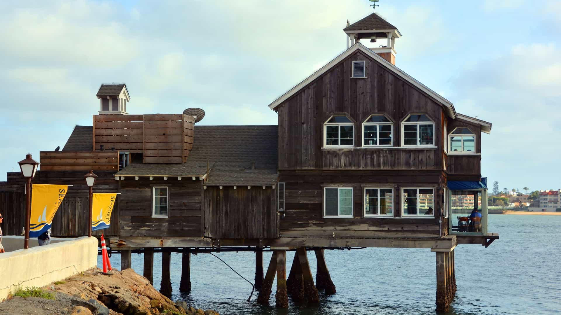 A bright, panoramic view of the San Diego, California skyline, featuring a cluster of modern downtown high rise buildings along the waterfront. In the foreground, the San Diego Bay is visible, likely containing a marina with moored boats, captured under a clear sky.