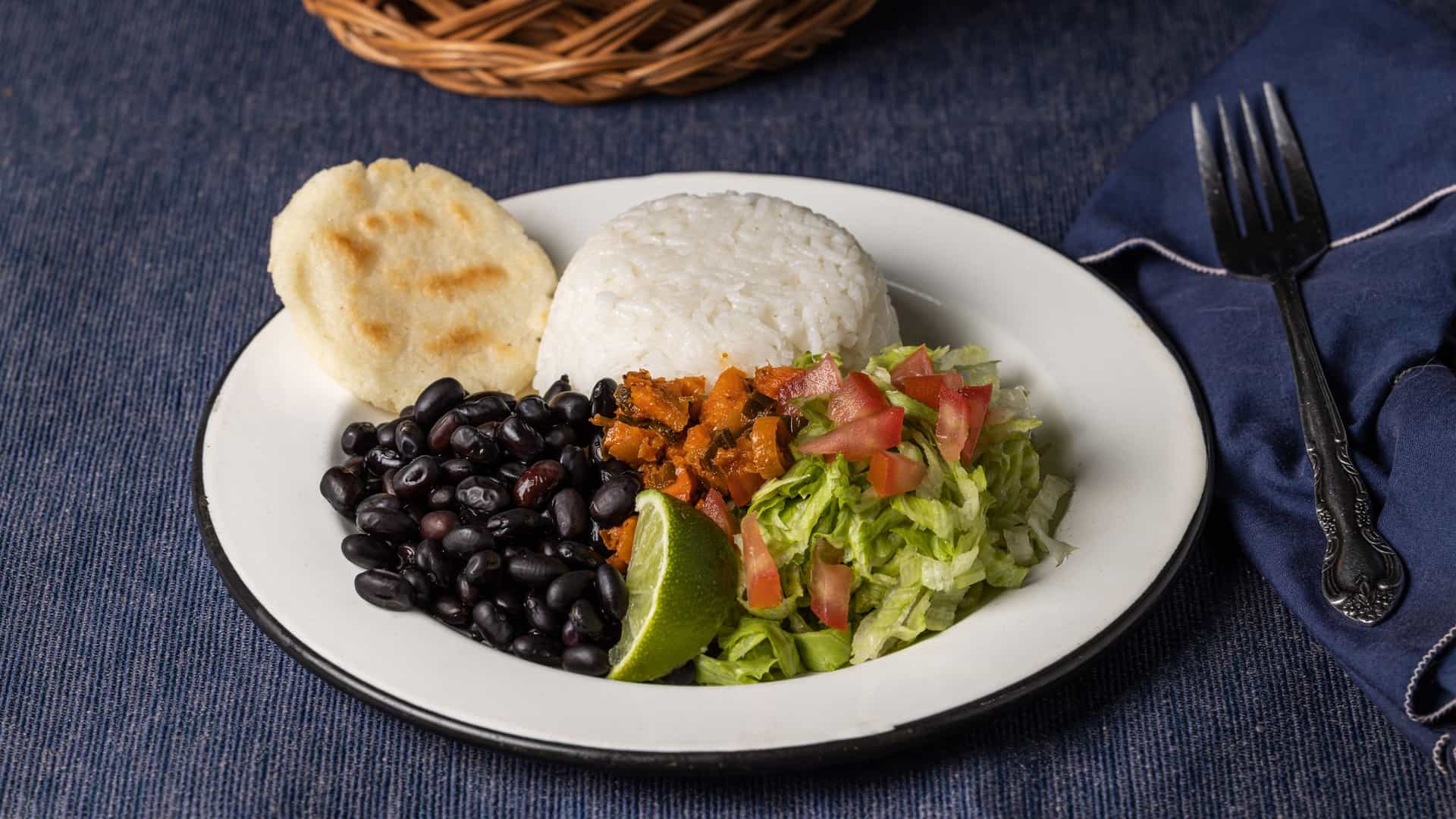  A colorful Casado, a typical Costa Rican lunch, served on a plate and composed of several distinct components: white rice, black beans, a main protein (such as meat, chicken, or fish), fried sweet plantains, and a fresh side salad.