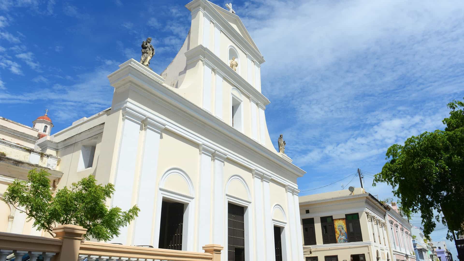  The exterior of the Cathedral of San Juan Bautista in Old San Juan, Puerto Rico, showcasing its Neoclassical facade with a domed central entrance and twin bell towers, under a blue sky. The cathedral is one of the oldest religious buildings in the Americas.