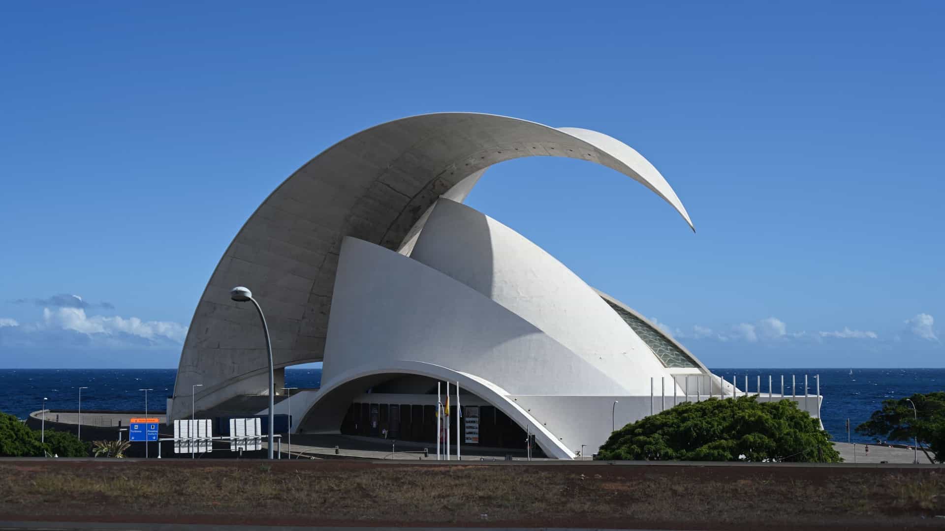  The iconic Auditorio de Tenerife "Adán Martín," a dramatic white concrete concert hall designed by Santiago Calatrava, featuring a massive, sweeping, wing like roof that arches over the main structure. The modern building stands prominently on a waterfront plaza overlooking the blue Atlantic Ocean in Santa Cruz de Tenerife, Canary Islands, Spain.