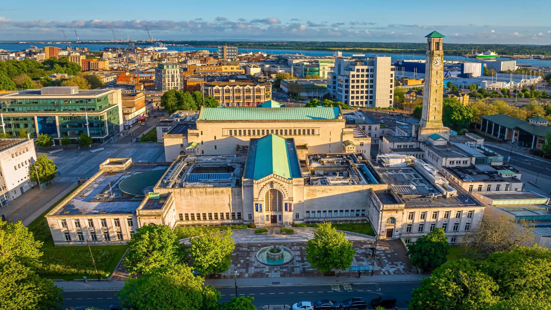  An aerial view of the SeaCity Museum in Southampton, England, showing the distinctive architecture of the Civic Centre building, which includes the tall, beige Clock Tower. The surrounding urban landscape is visible, with the Southampton Port and docks extending into the background.
