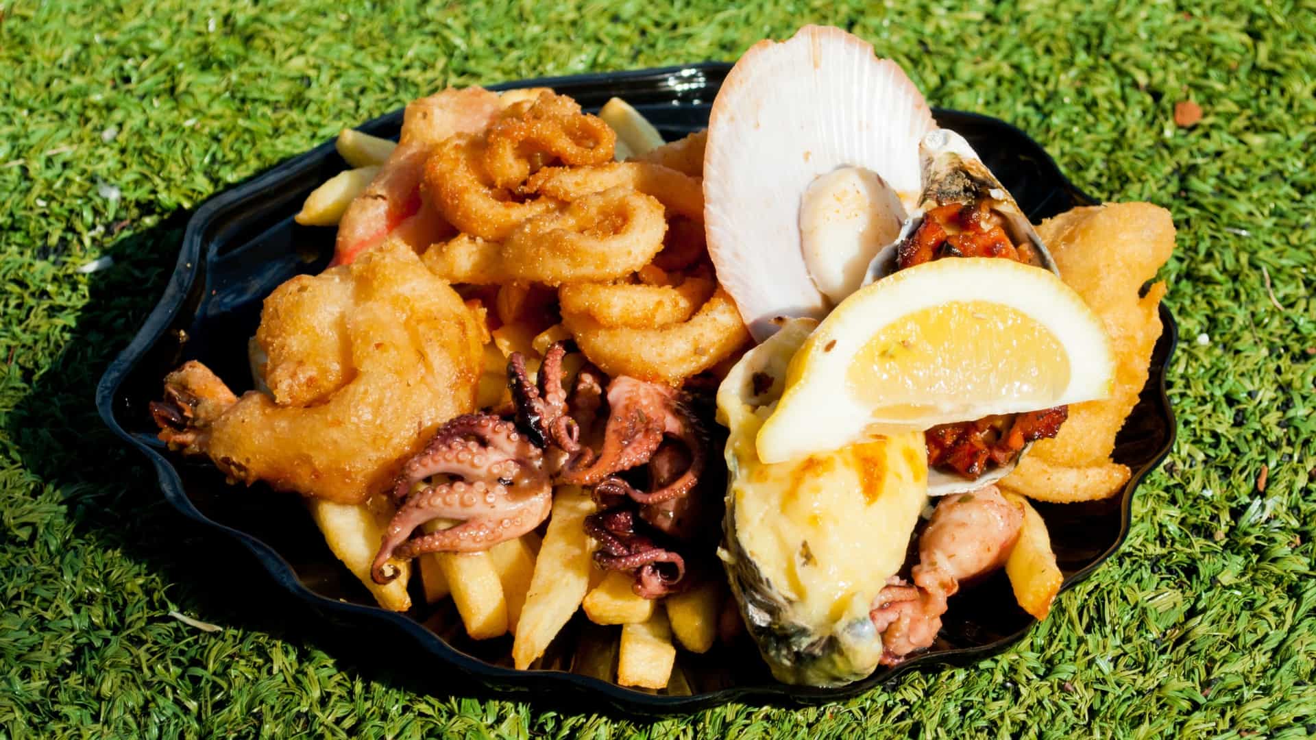  A close up of a fresh, prepared seafood dish or platter, likely purchased at the Sydney Fish Market. The platter is laden with a variety of seafood, including large cooked prawns, fresh oysters on the half shell, and possibly fried or grilled pieces of fish, garnished with lemon wedges.