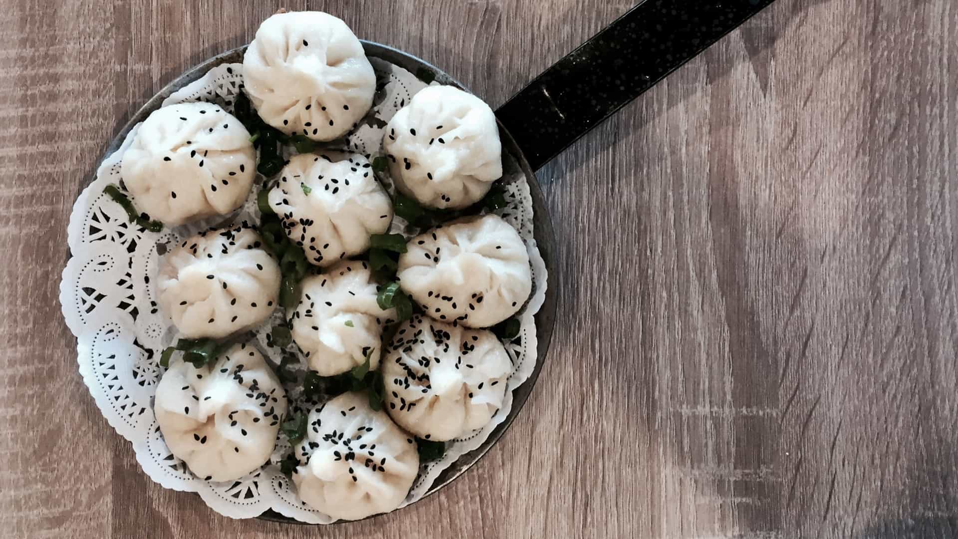  A close up view of several Goubuli Baozi (steamed, stuffed buns) from Tianjin, China, arranged on a plate. The buns have a smooth, white, slightly glossy exterior and are characterized by the delicate, pinched pleats on their tops, which are traditionally made with exactly eighteen folds.
