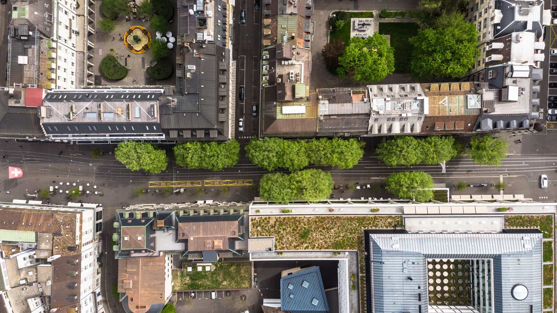  top down aerial view of the Bahnhofstrasse in the heart of Zurich, Switzerland. The image looks directly down onto the street, showcasing the broad, tree lined avenue, with tram tracks running down the center. It highlights the surrounding density of the financial district and Old Town buildings.