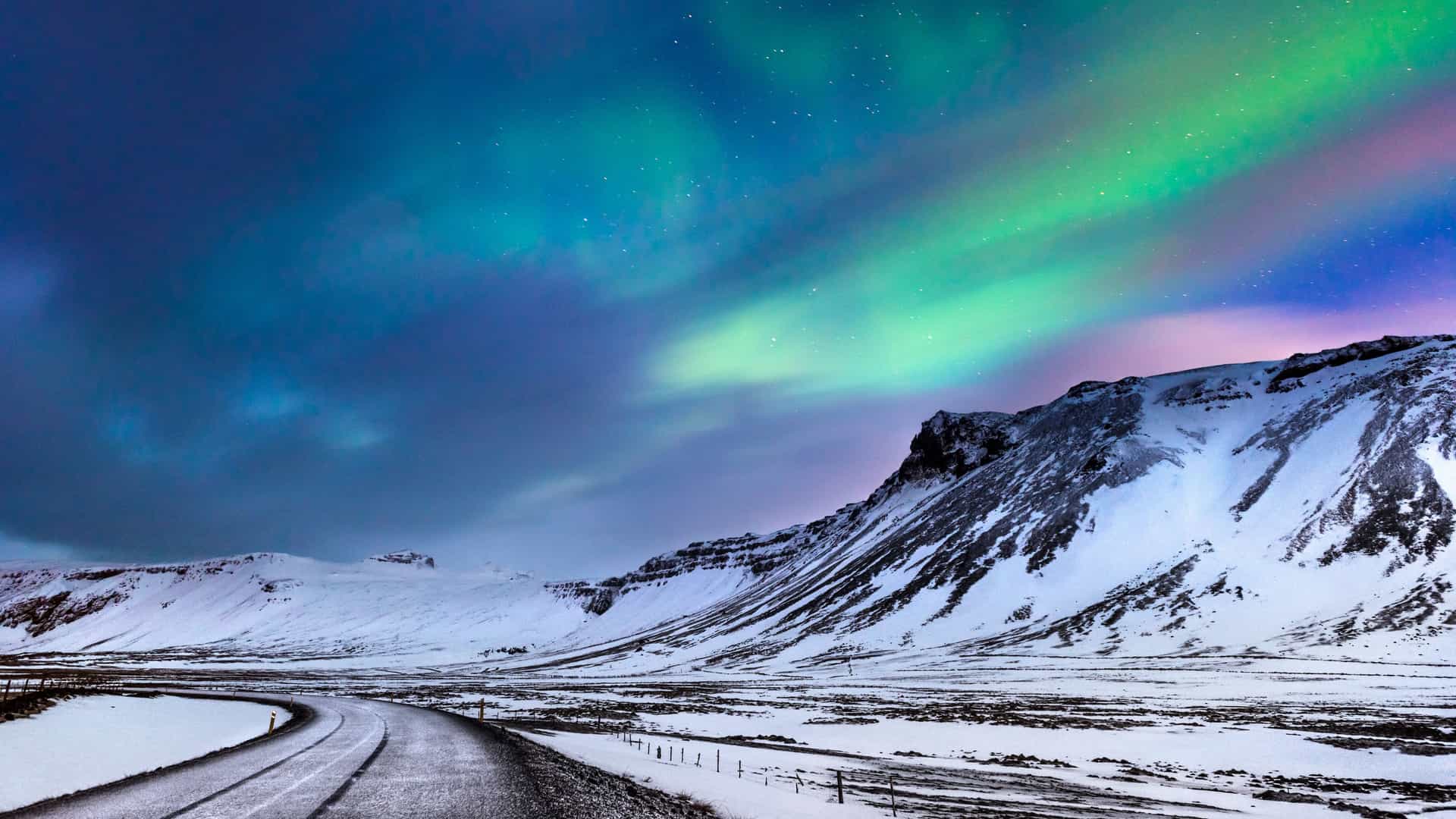 Explora journey view of the northern lights glowing over snowy mountains and a road in the Arctic Circle.
