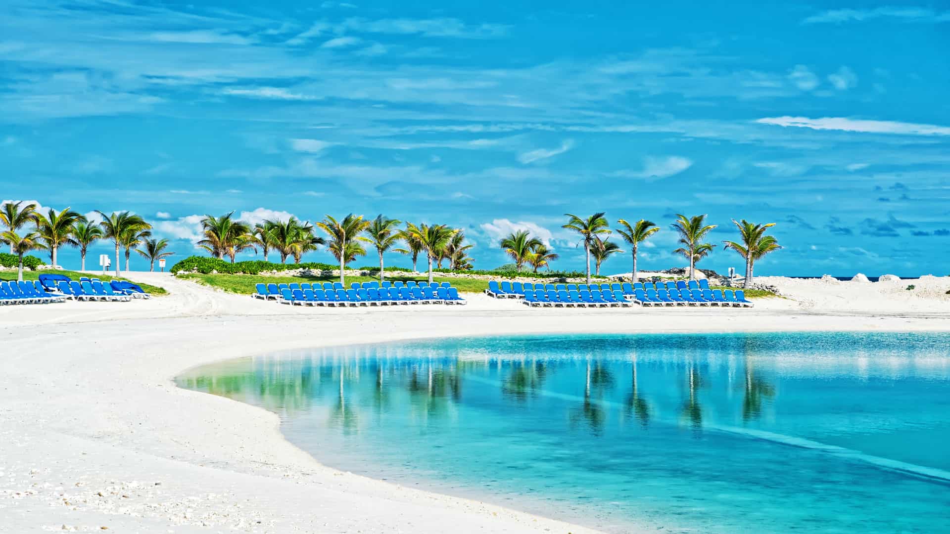 Explora journey view of a sunny white sand beach with turquoise water and lounge chairs in the Bahamas.