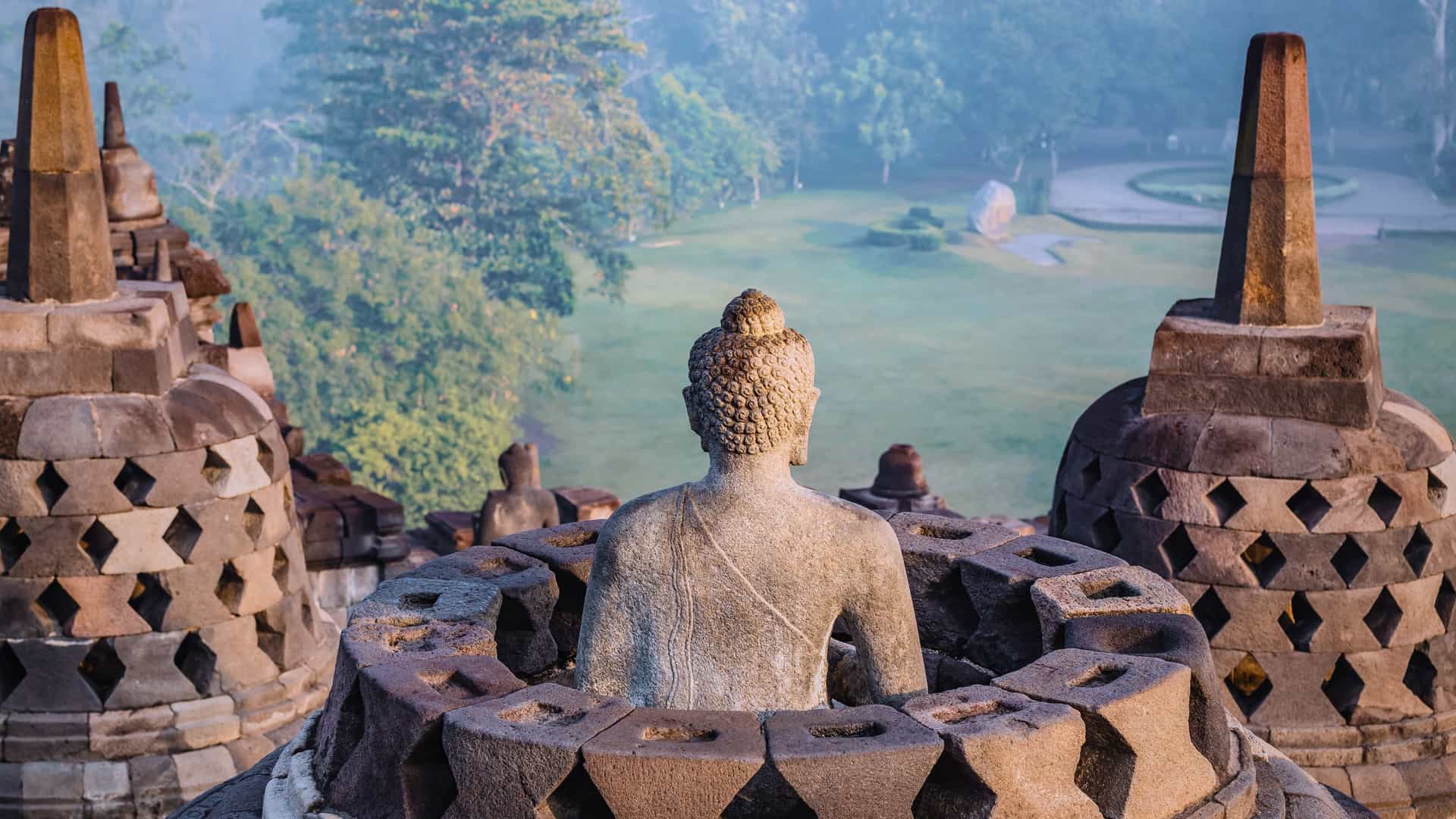 Explora journey view of a Buddha statue and stone stupas at the Borobudur temple in Southeast Asia.