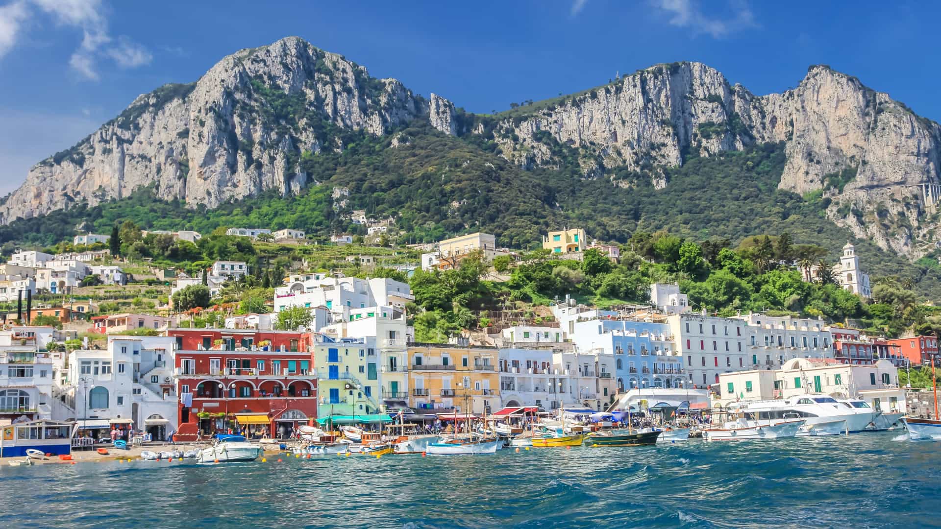 Explora journey view of colorful coastal buildings and boats under dramatic cliffs in Capri, Italy, Europe.