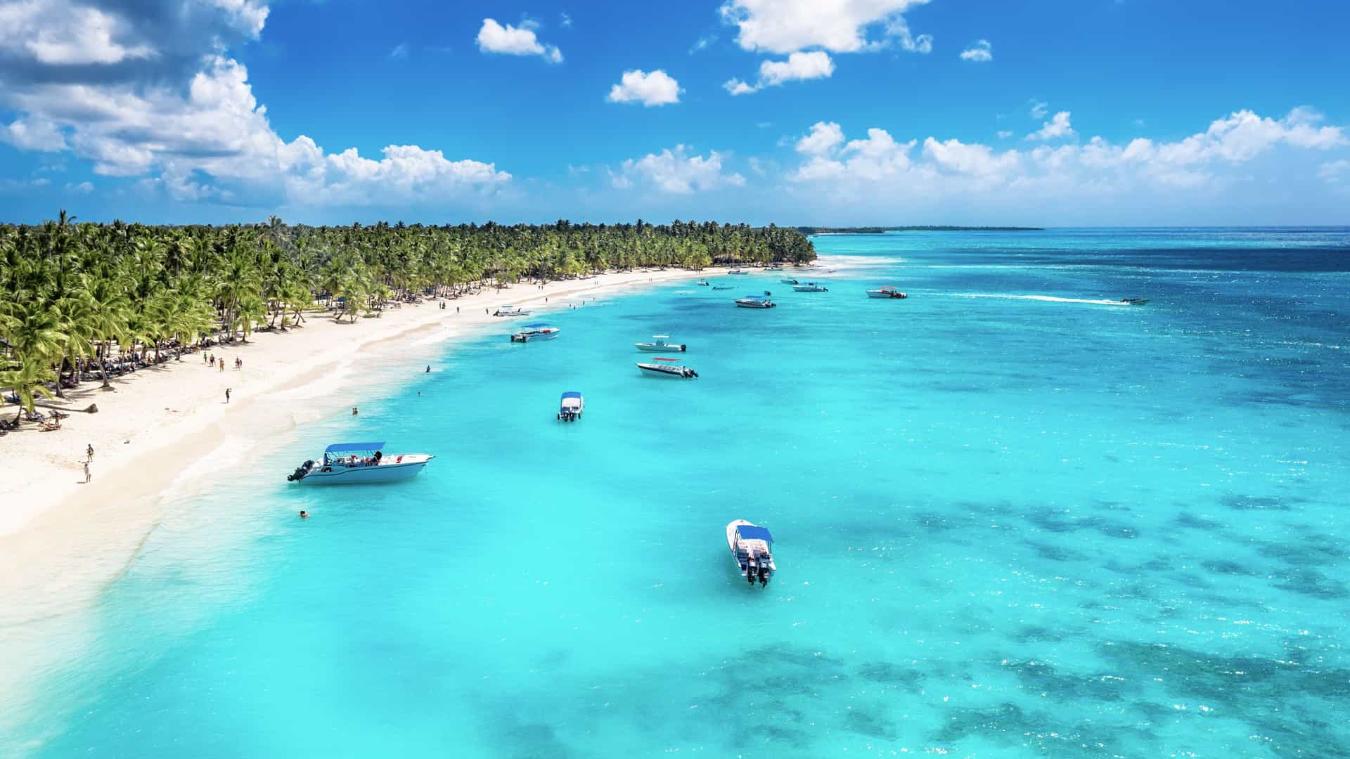 Explora journey view of a tropical Caribbean beach with crystal-clear turquoise water, white sand, and boats.
