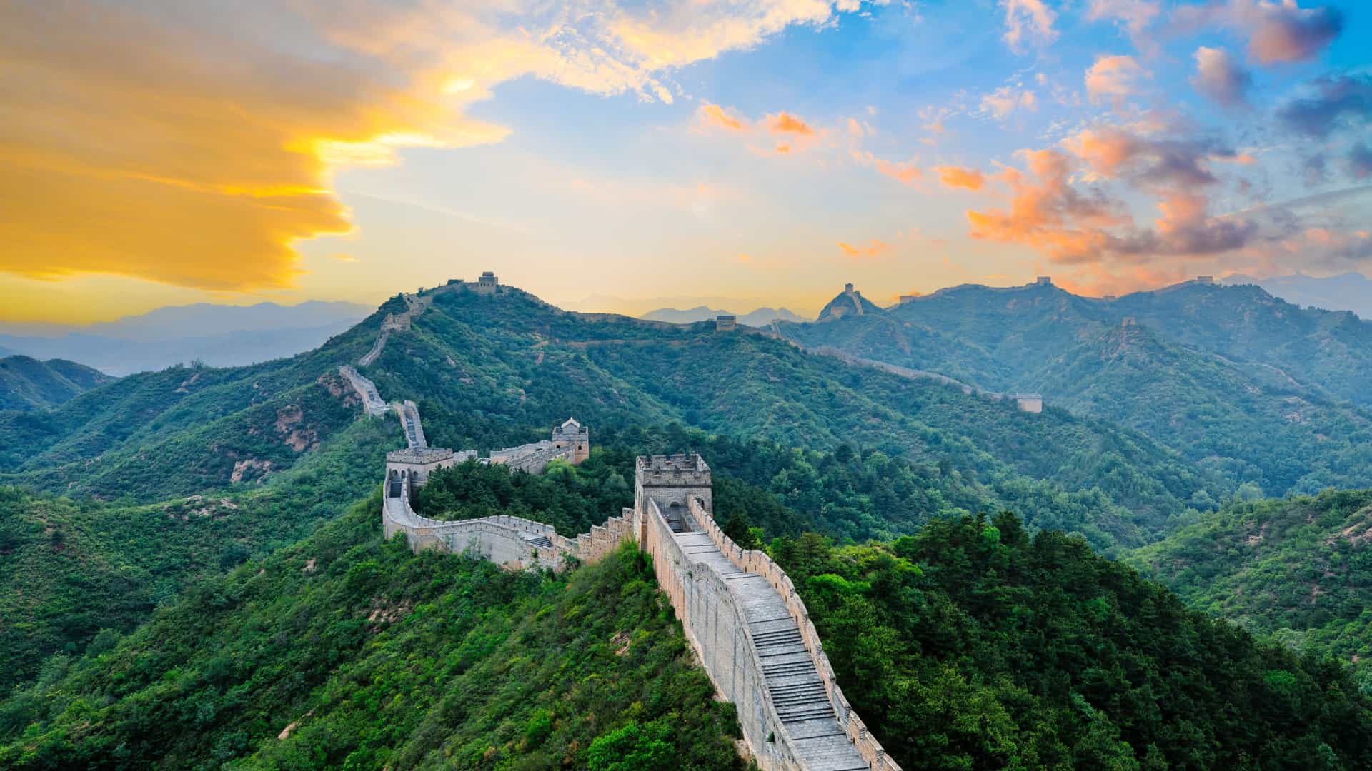 Explora journey view of the Great Wall of China winding across lush green mountains at sunset.