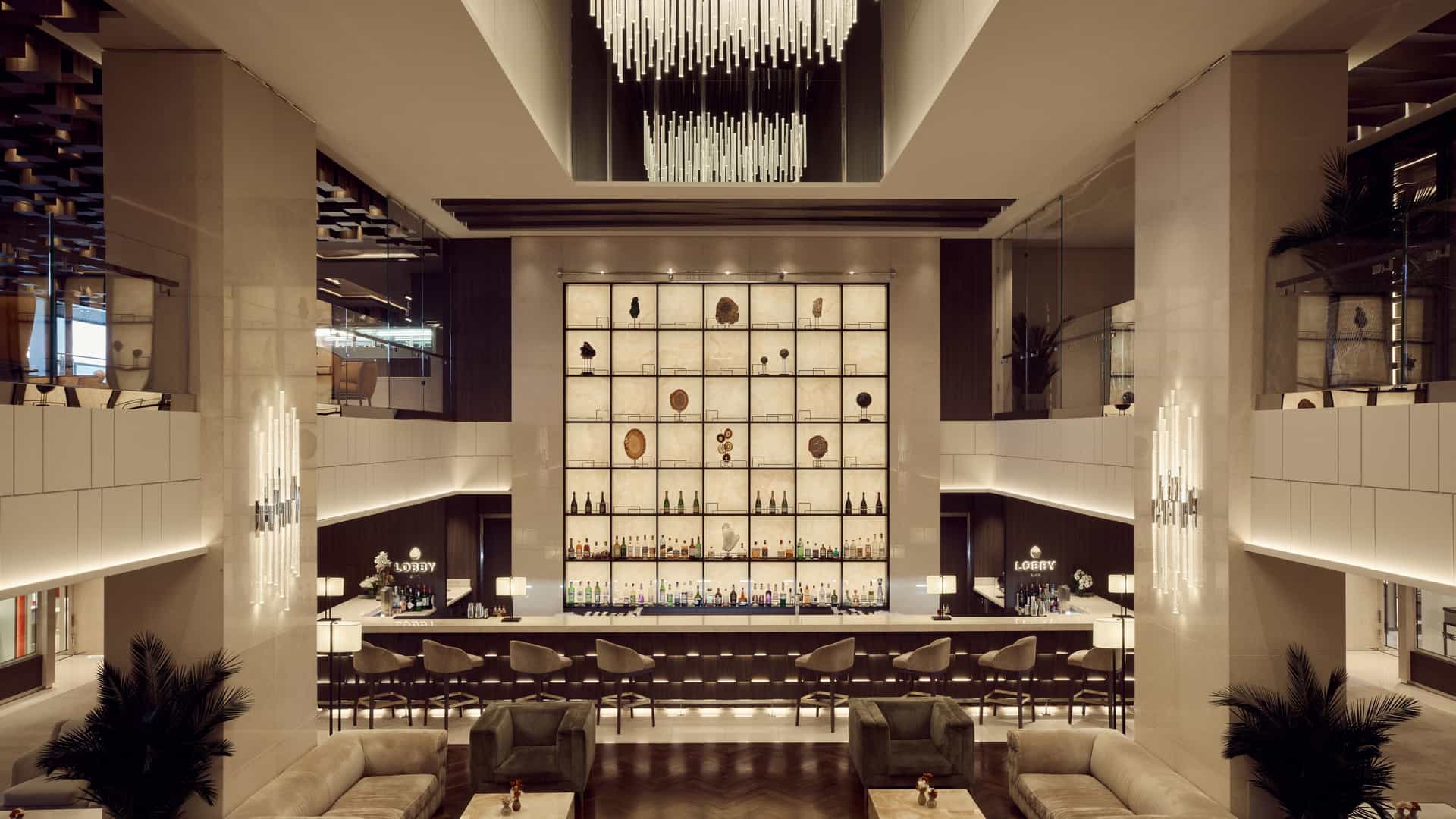 The lobby bar onboard the Explora 2, featuring a large illuminated wall with glass shelves featuring high-end bottles of spirits.