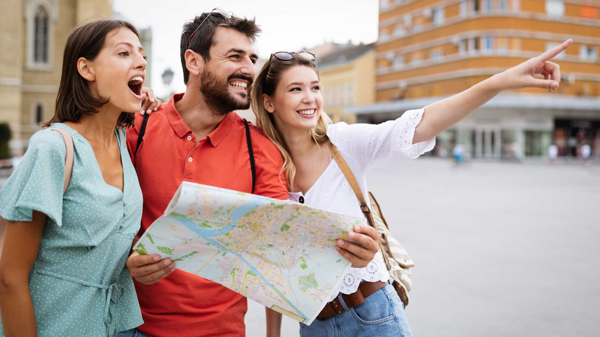 Three friends are outdoors, pointing at a map together while discussing where to go next.
