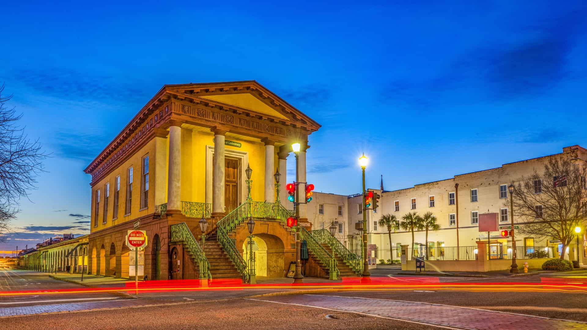 The historic yellow Market Hall in Charleston, South Carolina, captured at twilight with glowing street lamps and vibrant light trails from passing traffic.