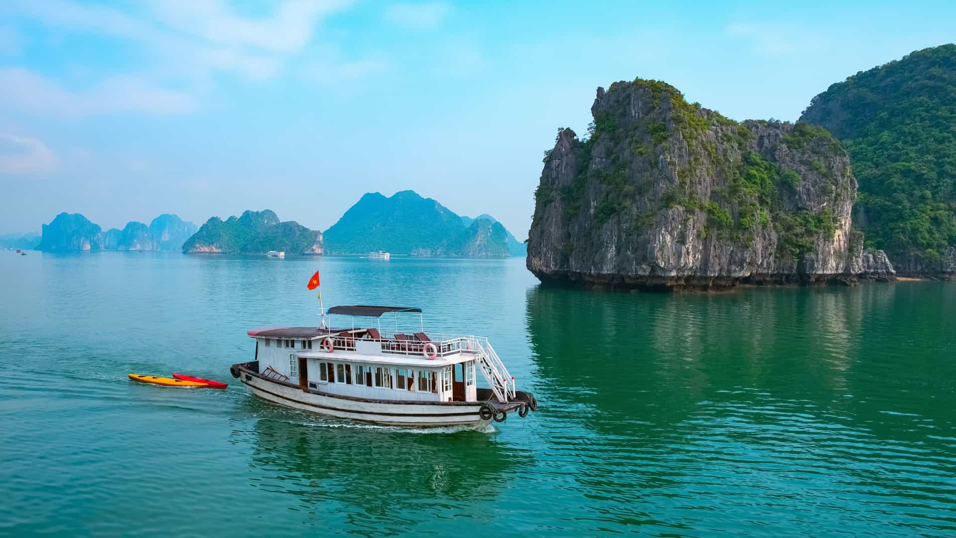 White boat with colorful kayak in Ha Long Bay’s calm, karst-lined waters—Holland America Southeast Asia cruise.
