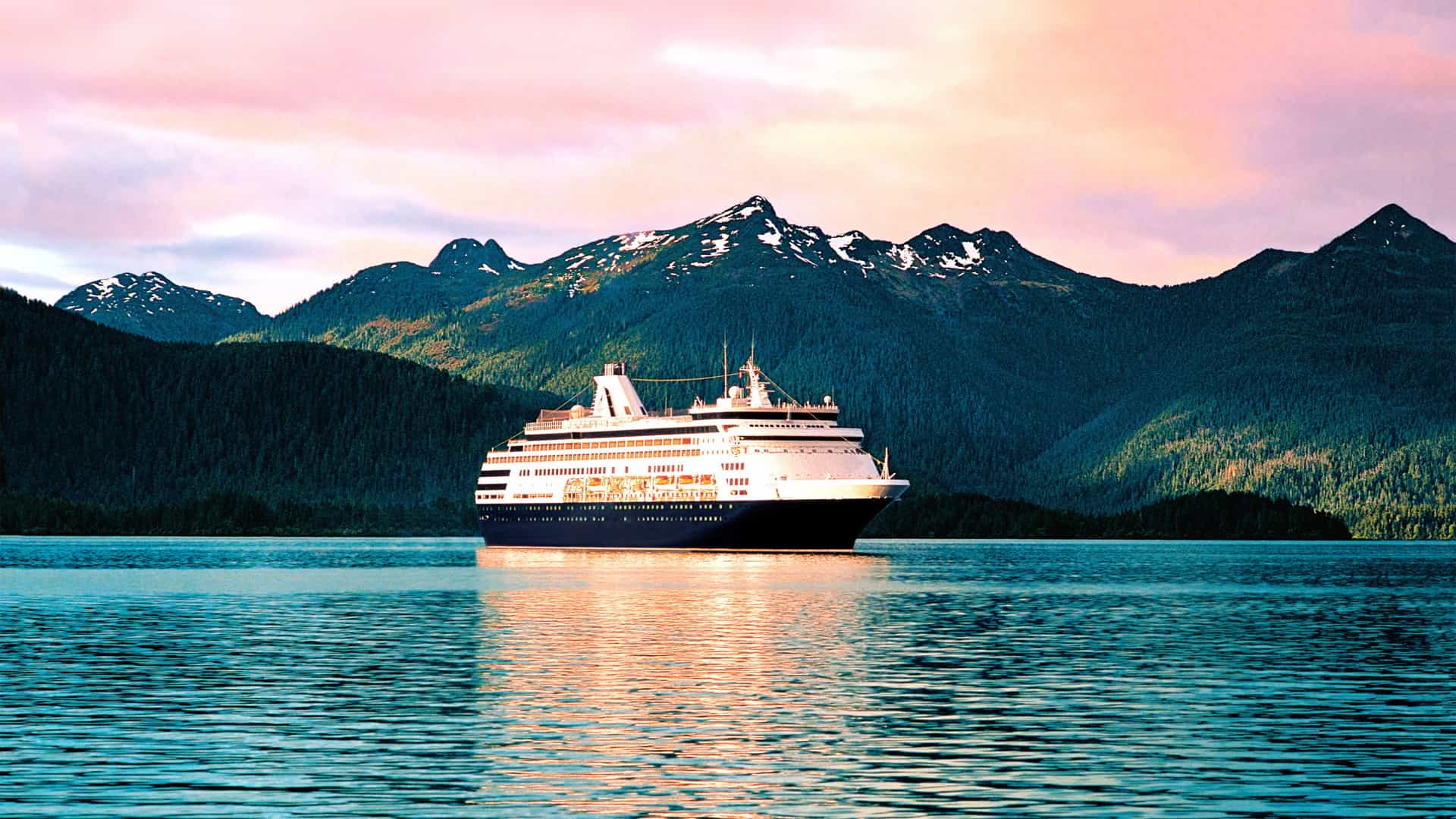 The Holland America cruise ship Westerdam embarks on a world cruise, sailing from Seattle with the city skyline and the snow-capped peak of Mount Rainier visible at sunset.