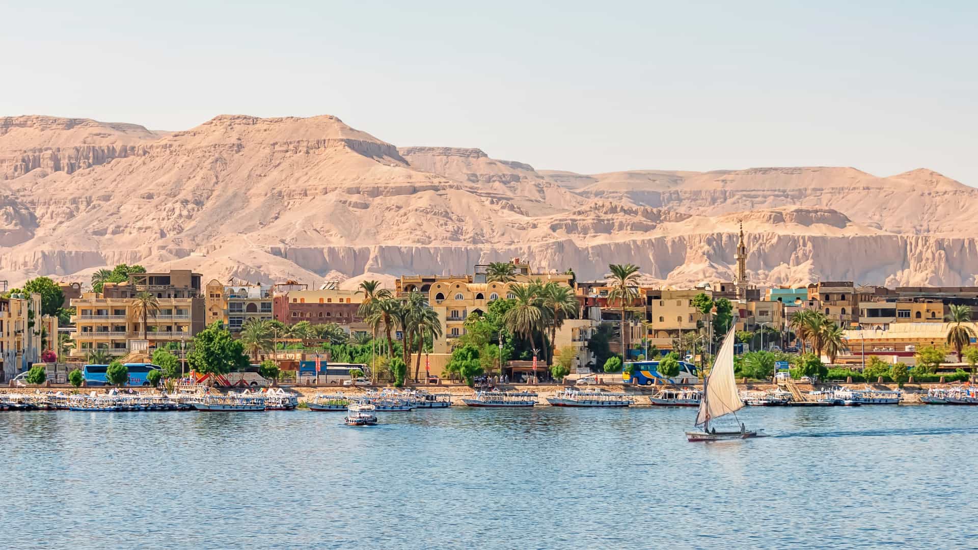 Panoramic view of Luxor, Egypt, with the Nile River, cityscape, arid mountains, and a Holland America Line cruise ship.