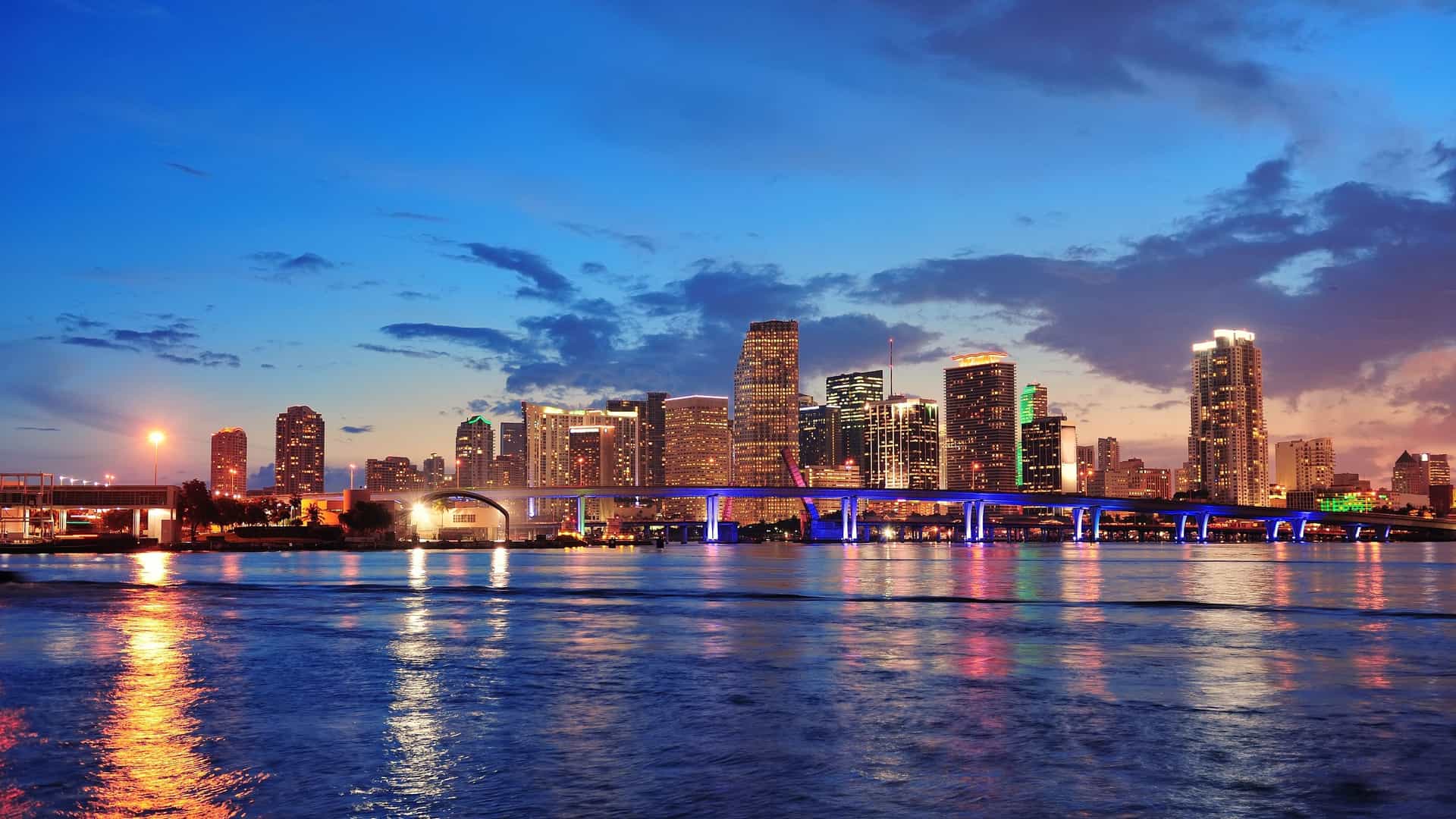 Miami skyline at dusk, showcasing vibrant colors and reflections shimmering in the water below.