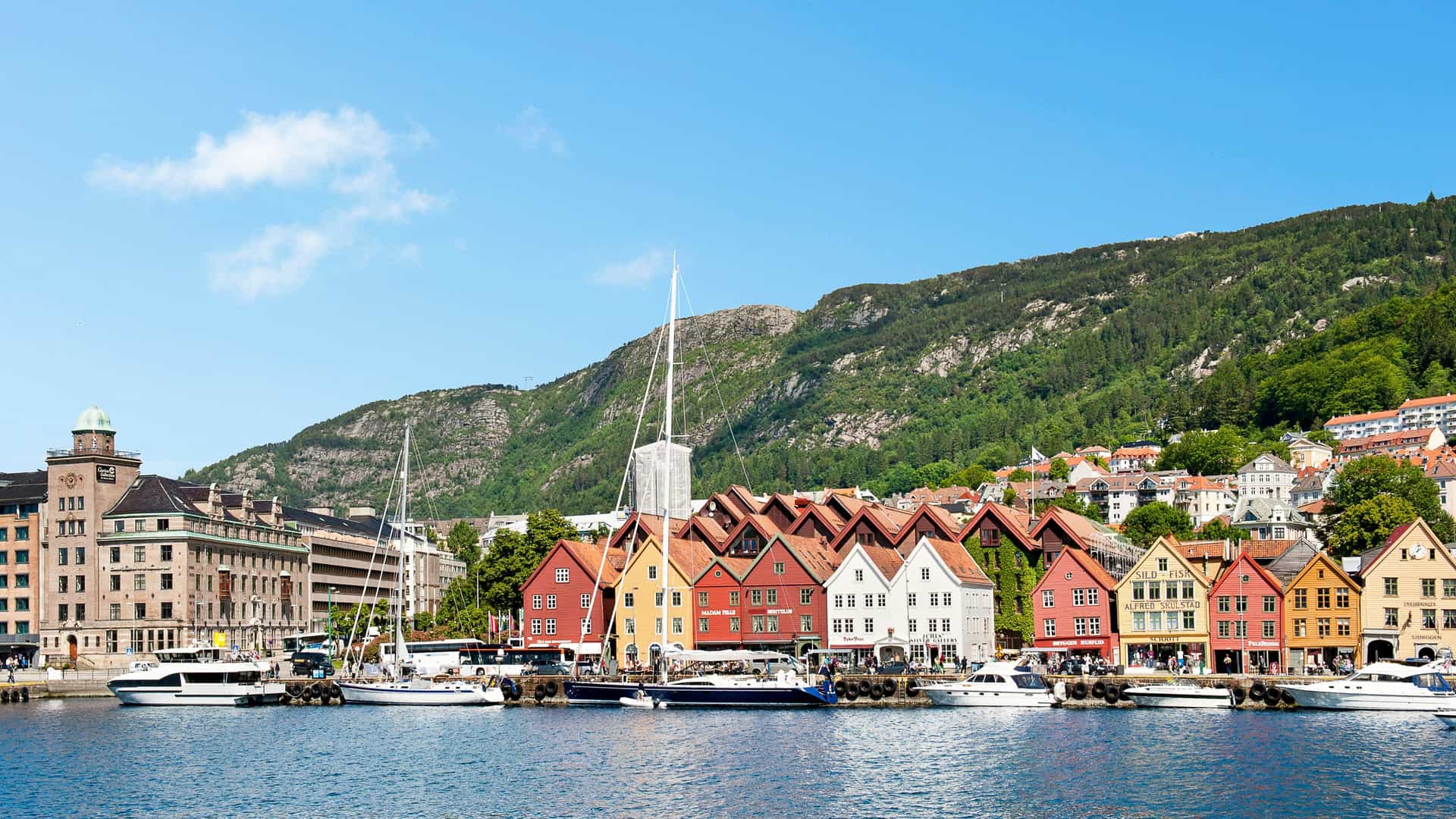 Colorful waterfront buildings and boats at the harbor in Bergen, Norway, Northern Europe, with green hills in the background.