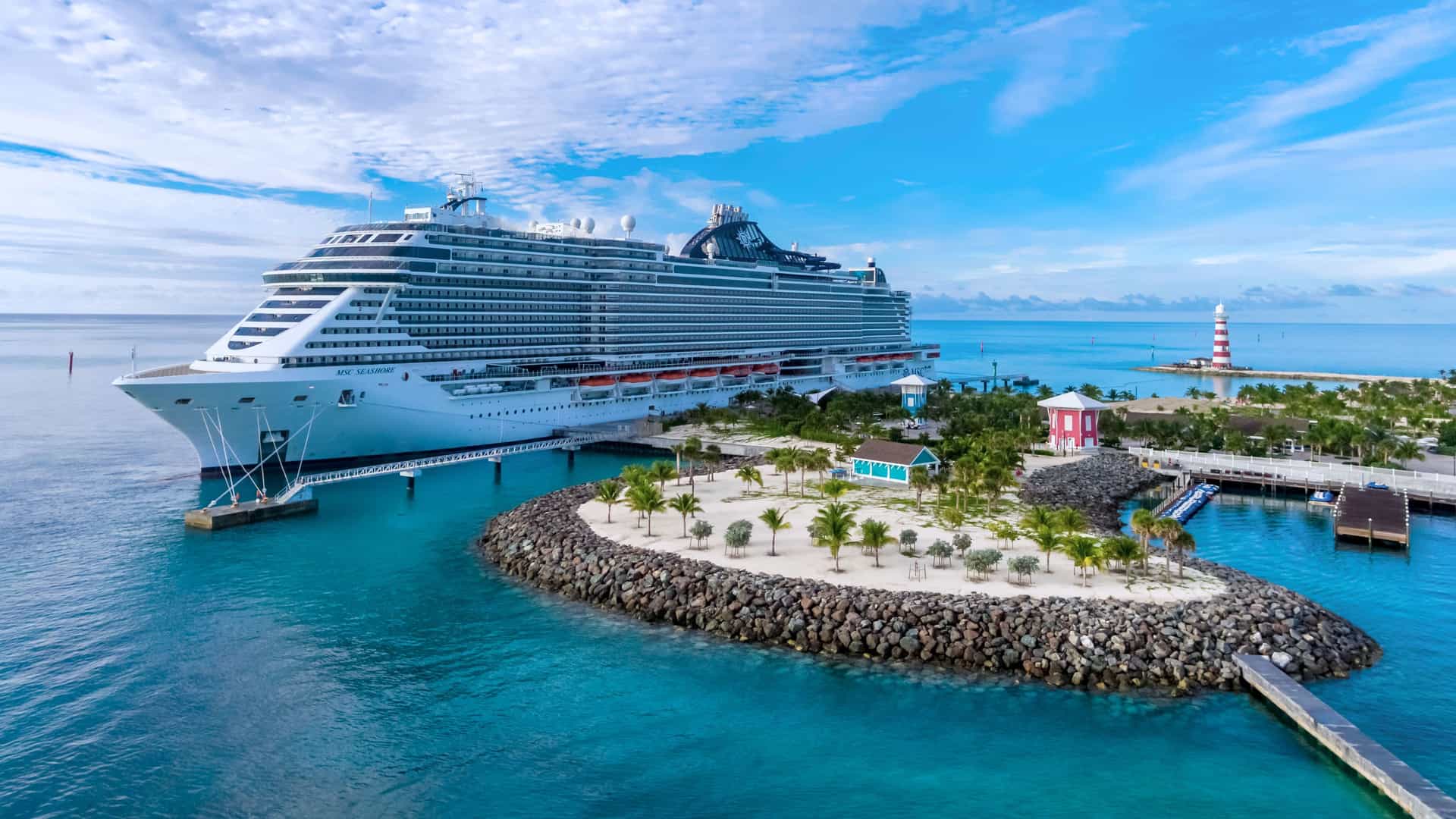 MSC cruise ship docked at Ocean Cay in the Bahamas, Antilles region, with palm trees, sandy beaches, and a red-and-white lighthouse.