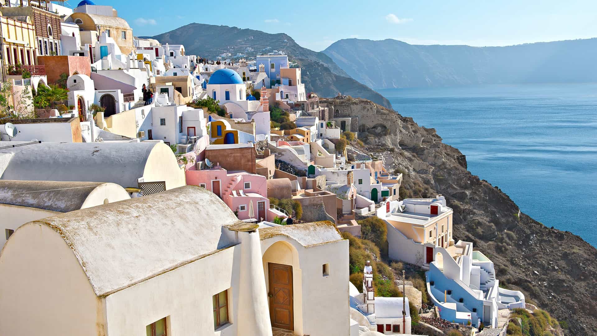 Whitewashed buildings with blue domes on a hillside in Santorini, Greece, Northern Europe, overlooking the sea and mountains.