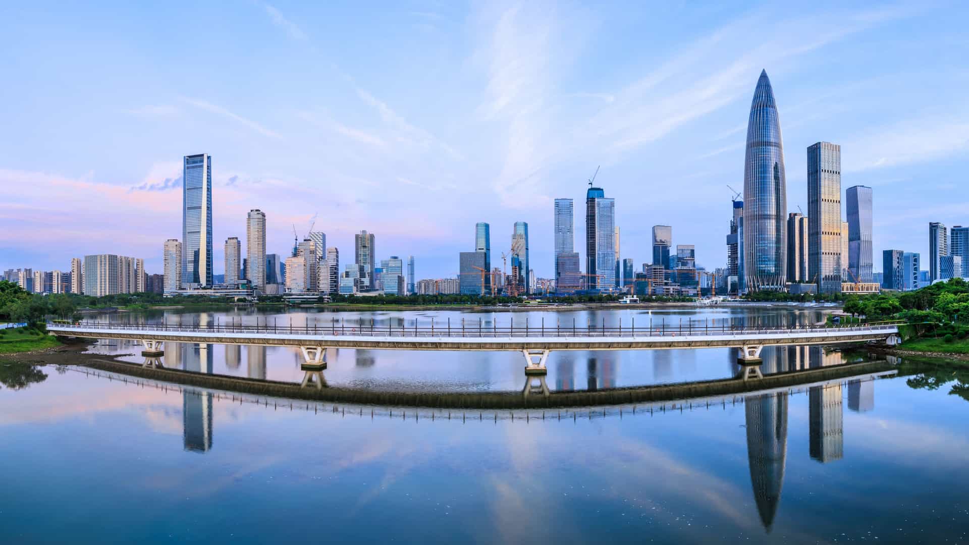 Panoramic view of the Shenzhen skyline in Northern Asia, with high-rise buildings, a bridge, and water reflections.