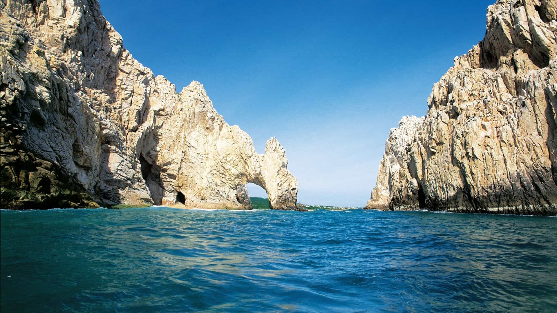 Norwegian Cruise Line ship approaching the iconic Land's End Arch (El Arco) in Cabo San Lucas, Mexico, showcasing the rugged rock formations and clear blue waters of the Mexican Riviera.