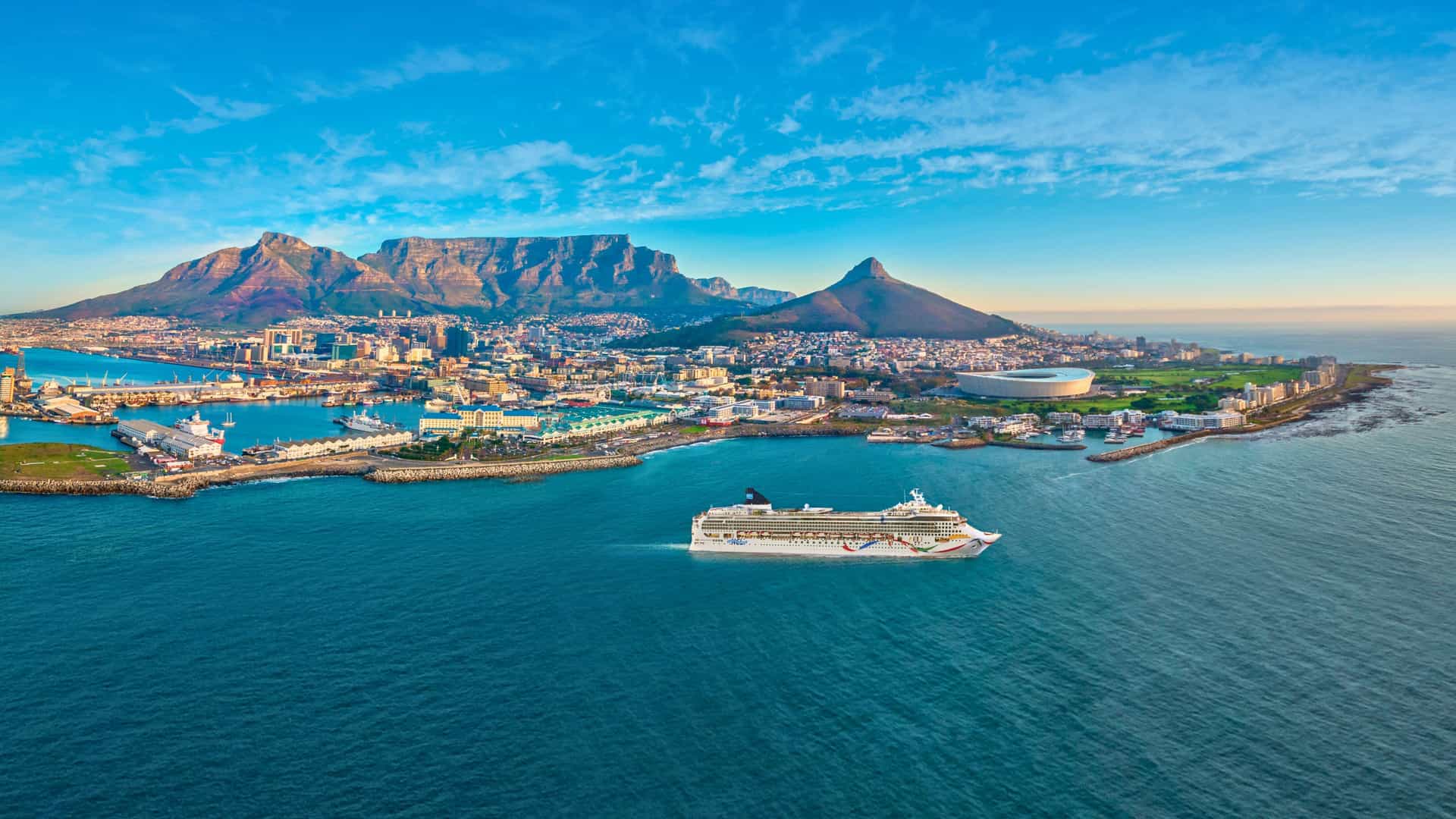 Aerial view of Norwegian Dawn cruise ship sailing from Cape Town, South Africa, with Table Mountain in the background. Explore diverse itineraries, including Holland America cruise options.