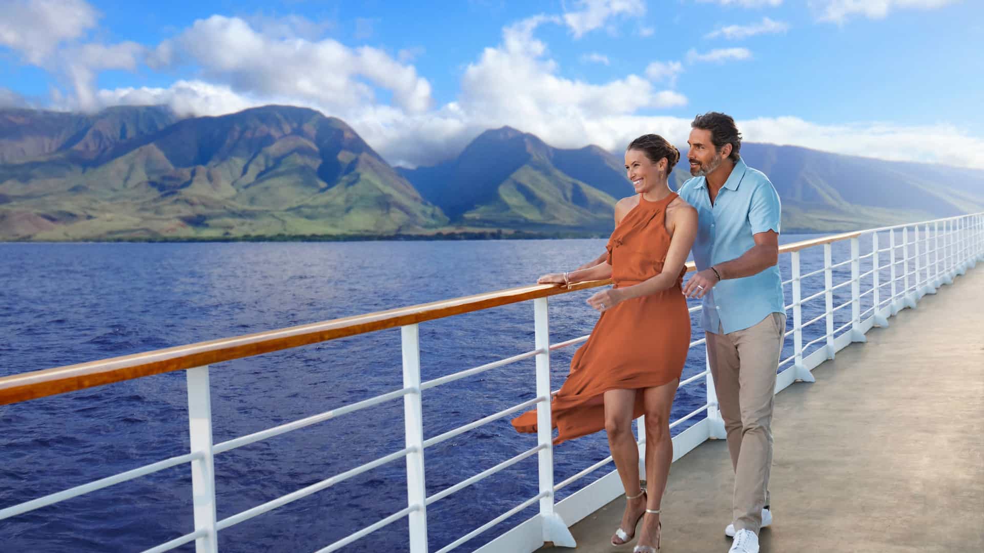 A couple on a Norwegian Cruise Line ship enjoying the stunning volcanic coastline of Maui, Hawaii, USA, with lush green mountains meeting the Pacific Ocean.