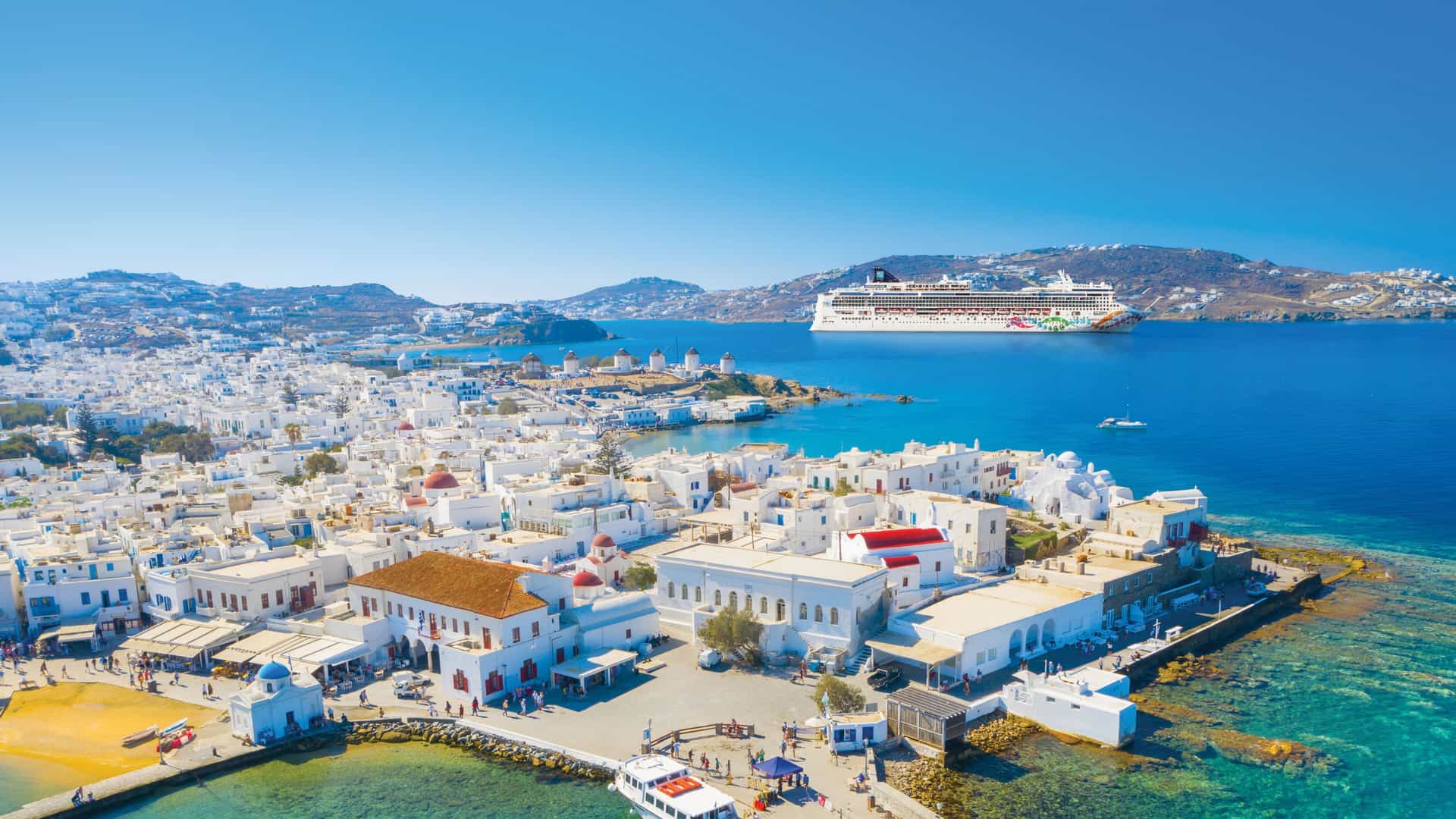 The Norwegian Cruise Line Pearl ship anchored near Mykonos, Greece, showcasing the iconic white-washed buildings and vibrant blue waters of this Mediterranean island.