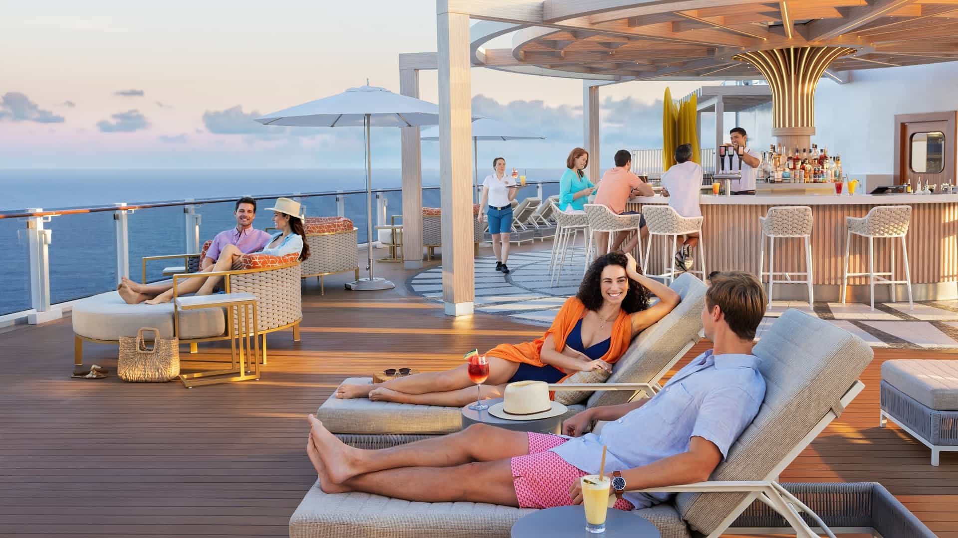 A couple is lounging on sunbeds near a bar on the Norwegian Cruise Line's Norwegian Luna ship at sunset, with the man and woman facing each other while drinking colorful cocktails.