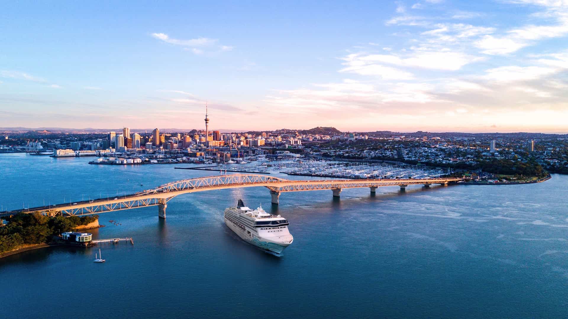 The Norwegian Cruise Line Spirit ship arriving in Auckland, New Zealand, passing under the Harbour Bridge with the city skyline and Sky Tower in the background, during a Trans-Pacific cruise.