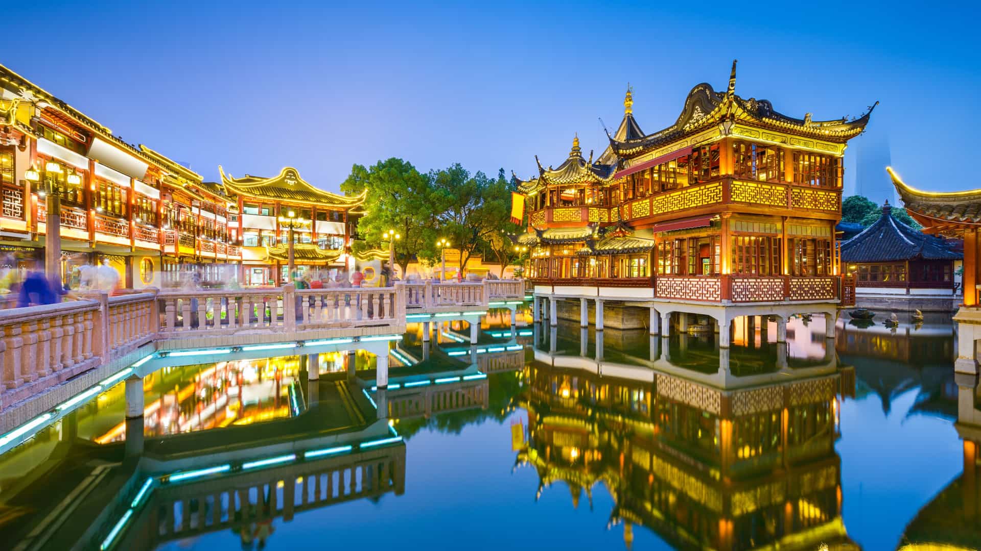 A stunning night view of the illuminated traditional Chinese buildings of Yu Garden in Shanghai, China, with their reflections on the water, a popular excursion for an Oceania cruise.