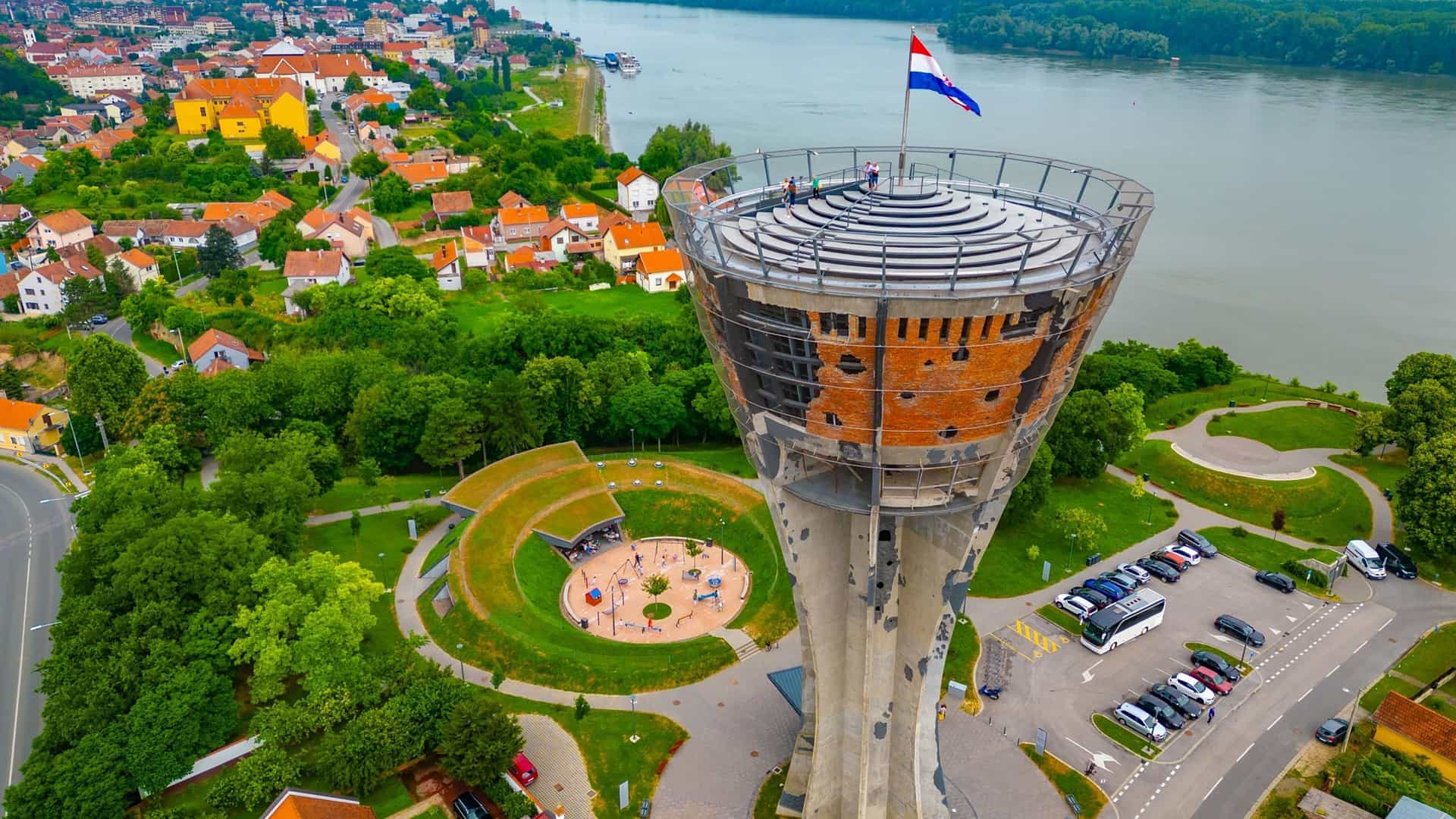 A wide-angle landscape shot of the Danube River with a boat passing under a bridge, and a picturesque town with colorful houses built along the riverbank in Aljmaš, Croatia.