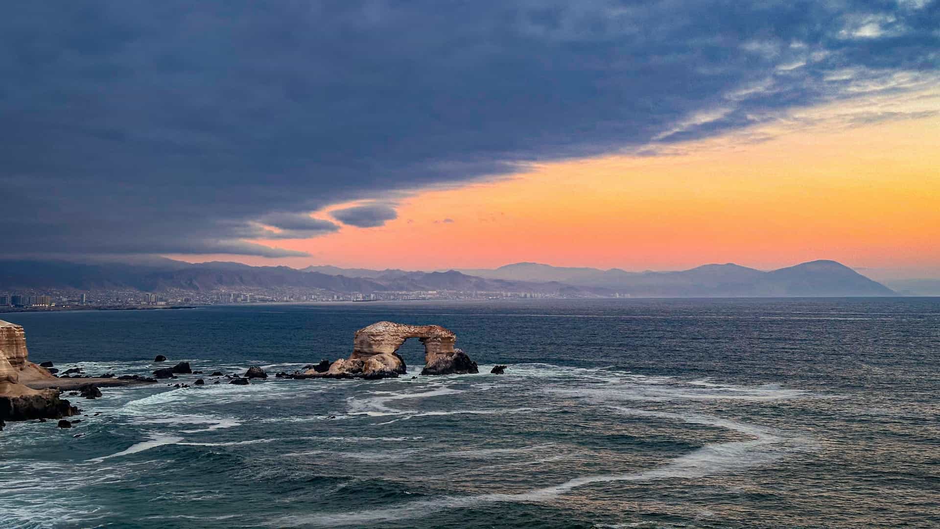 A view of a dense, hillside residential neighborhood in Antofagasta, Chile, where houses are painted in a vibrant, multicolored array. The brightly colored homes stand out against the pale, arid hillsides of the Atacama Desert region near the Pacific coast.